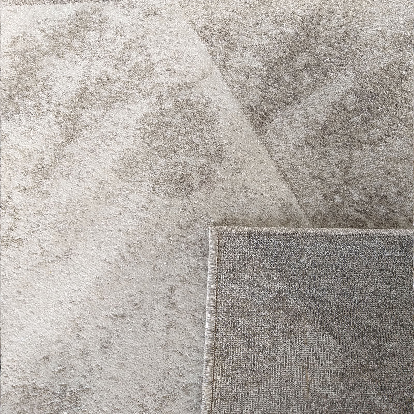 Tapis aux nuances de gris clair et beige avec un motif subtil effet usé, replié pour montrer son revers tissé
