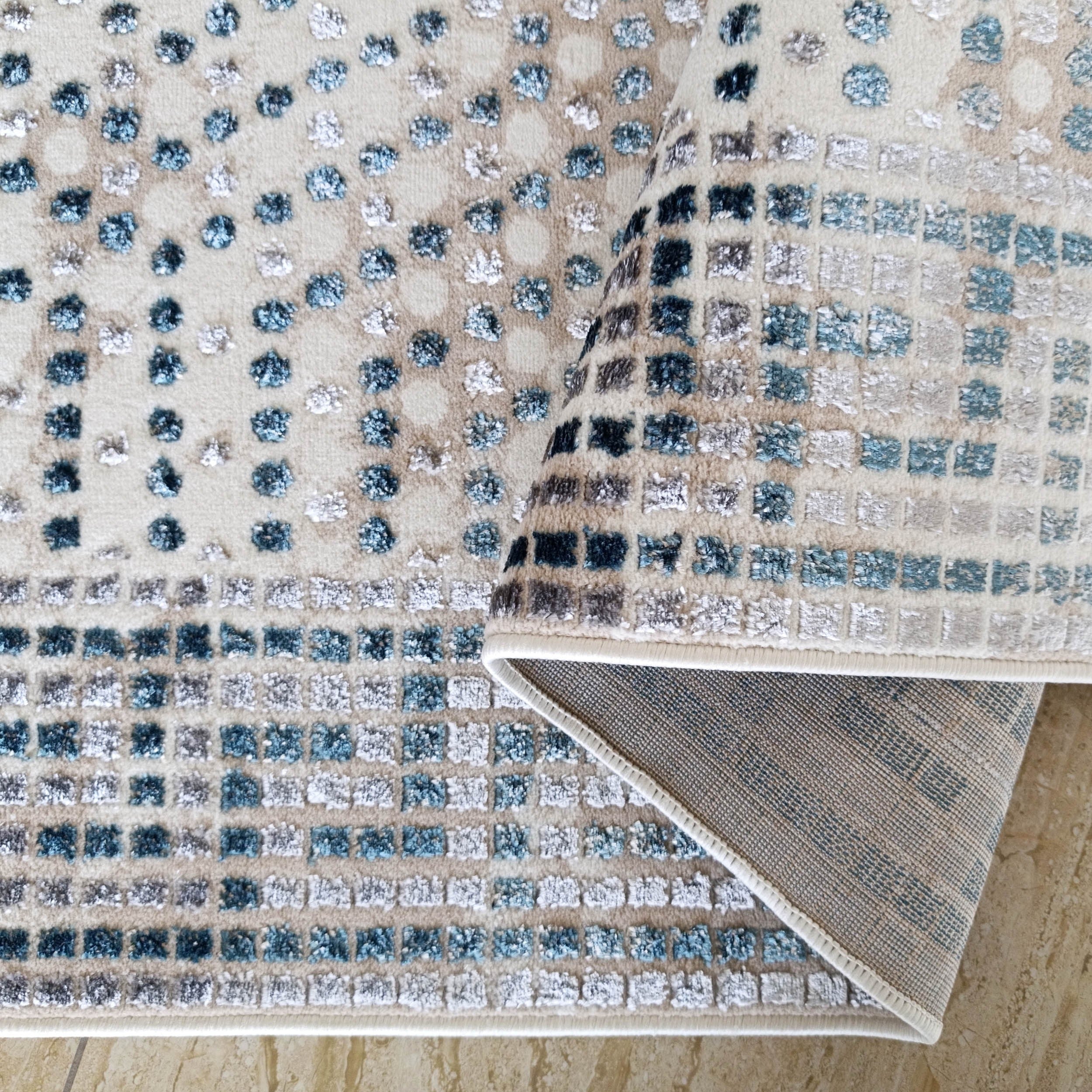 Tapis beige à motifs texturés en relief carrés et points bleu clair, foncé et blanc cassé sur carrelage