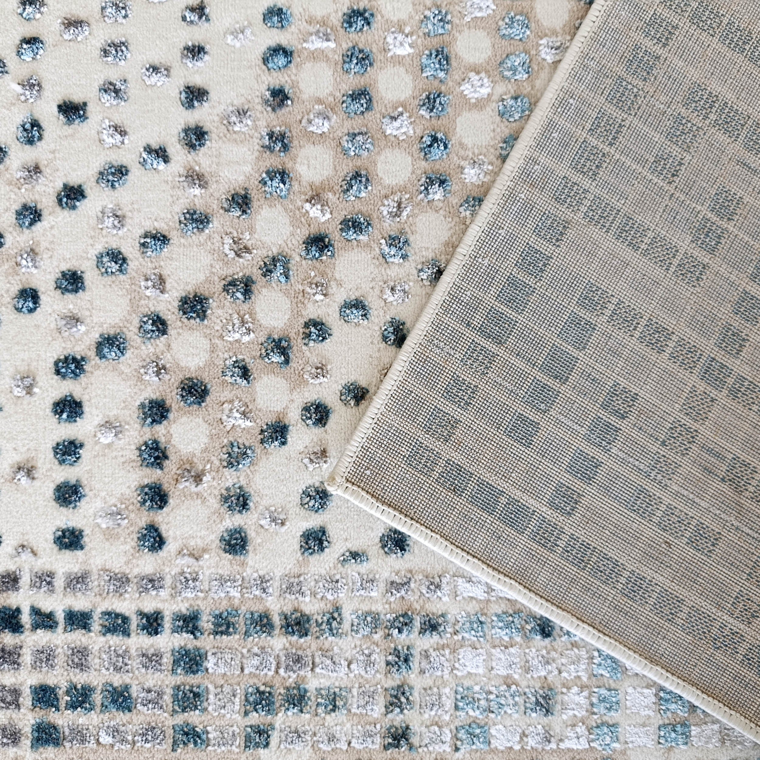 Tapis beige à motifs de points et carrés touffus bleus et gris. Le revers est une trame tissée beige quadrillée de bleu