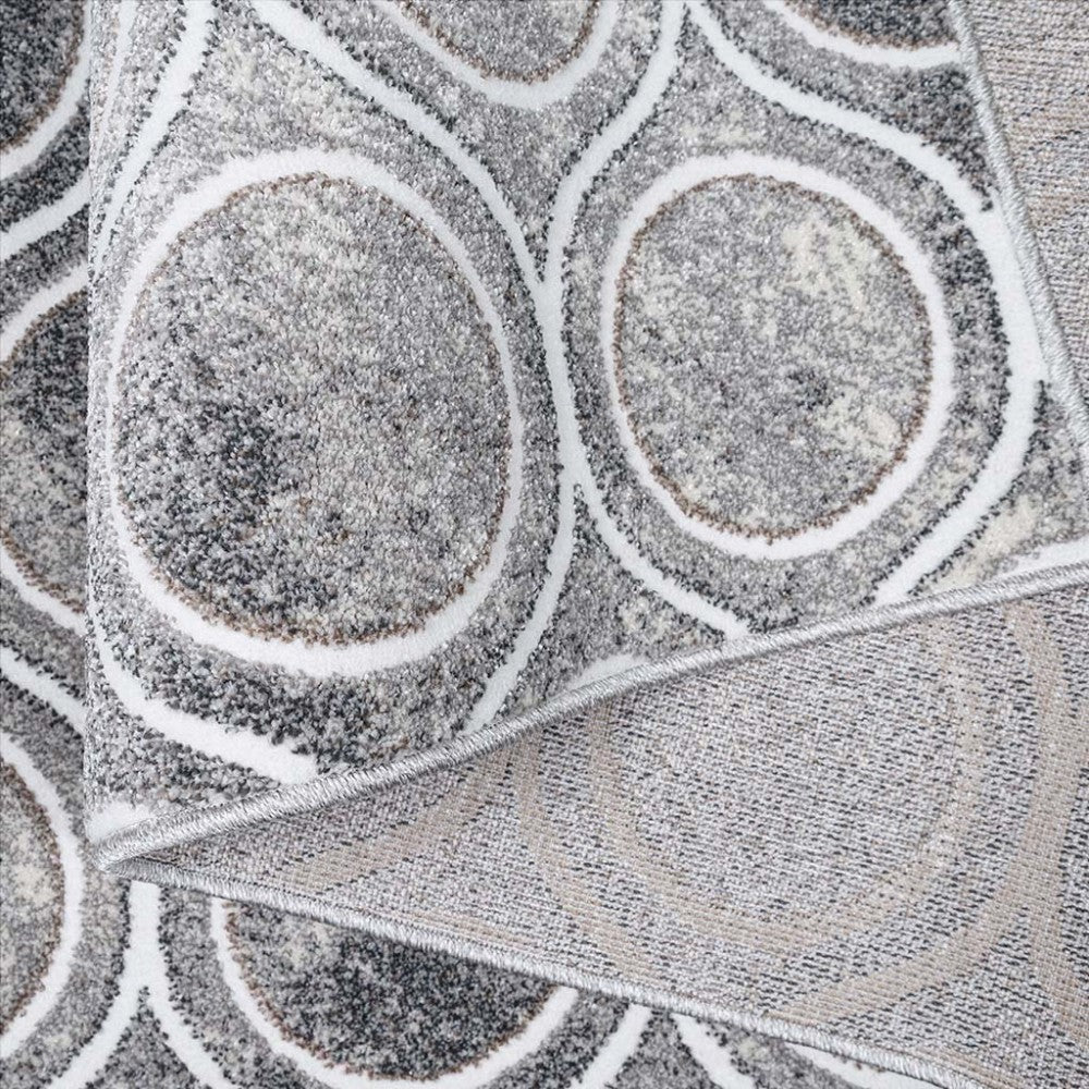 Tapis texturé gris et blanc avec un motif géométrique de cercles concentriques et entrelacés, montrant le dessus et un bord plié