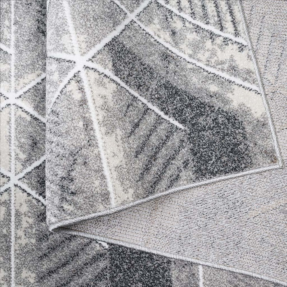 Tapis texturé à motifs géométriques blancs sur fond moucheté gris et noir, une partie est pliée