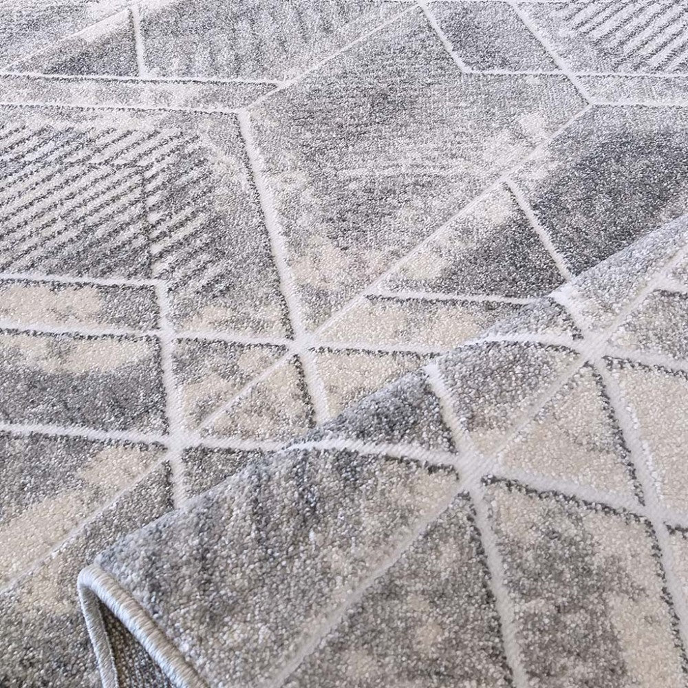 Tapis à motifs géométriques abstraits gris et blanc avec des lignes claires, à l'aspect doux et texturé, partiellement roulé