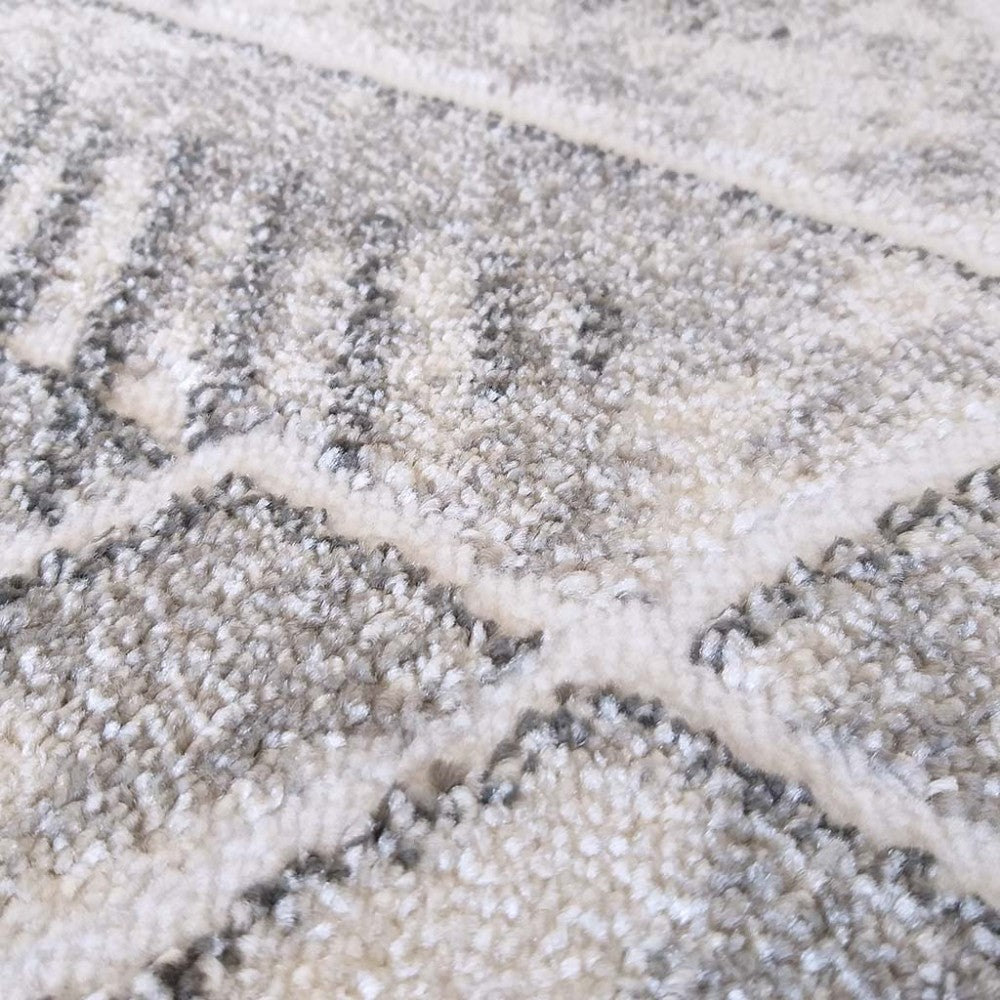 Tapis texturé à poils longs, présentant des motifs géométriques gris foncé sur un fond mélangé de gris clair et crème