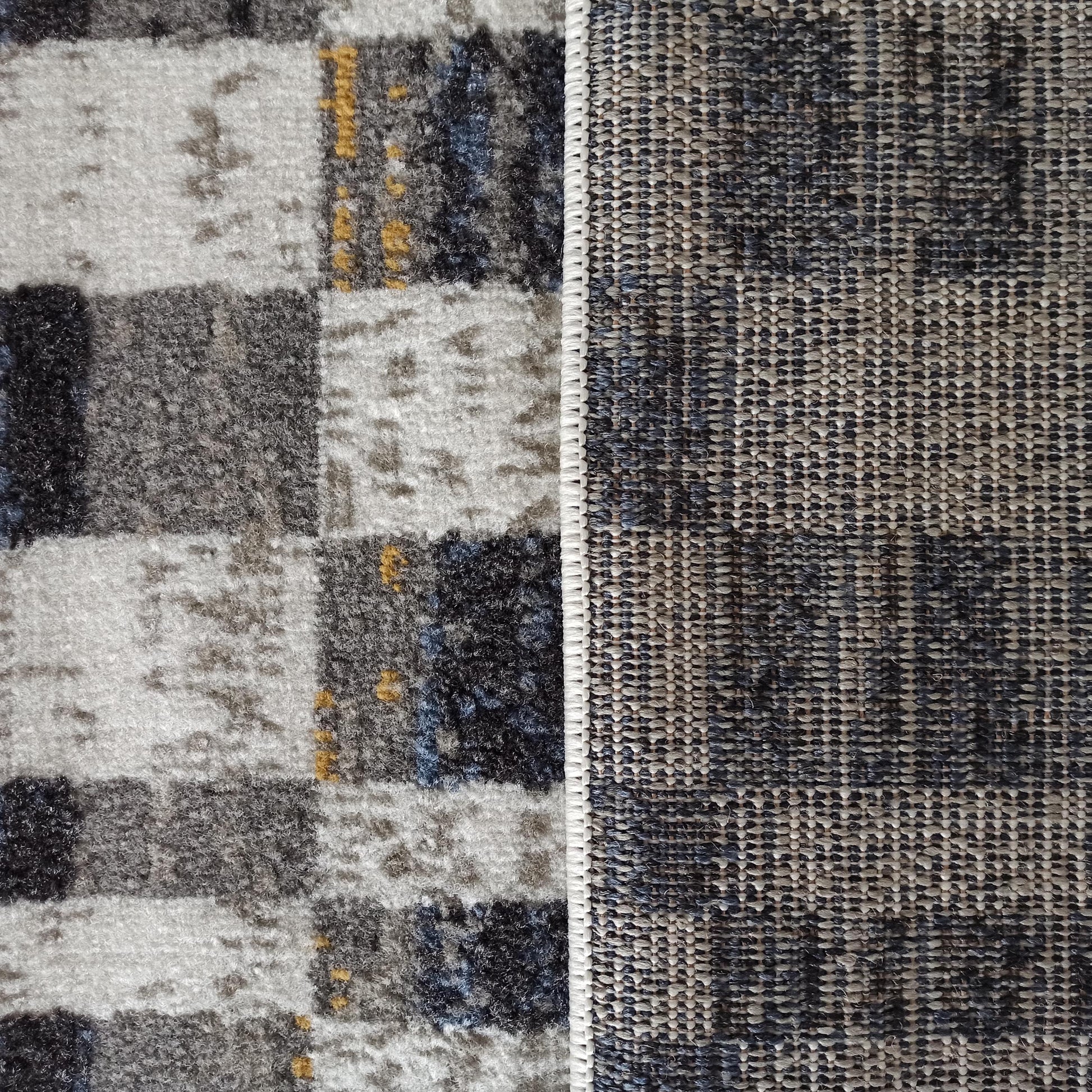 Tapis présentant une surface douce et mouchetée de gris, blanc, bleu et ocre, et son revers tissé à mailles serrées