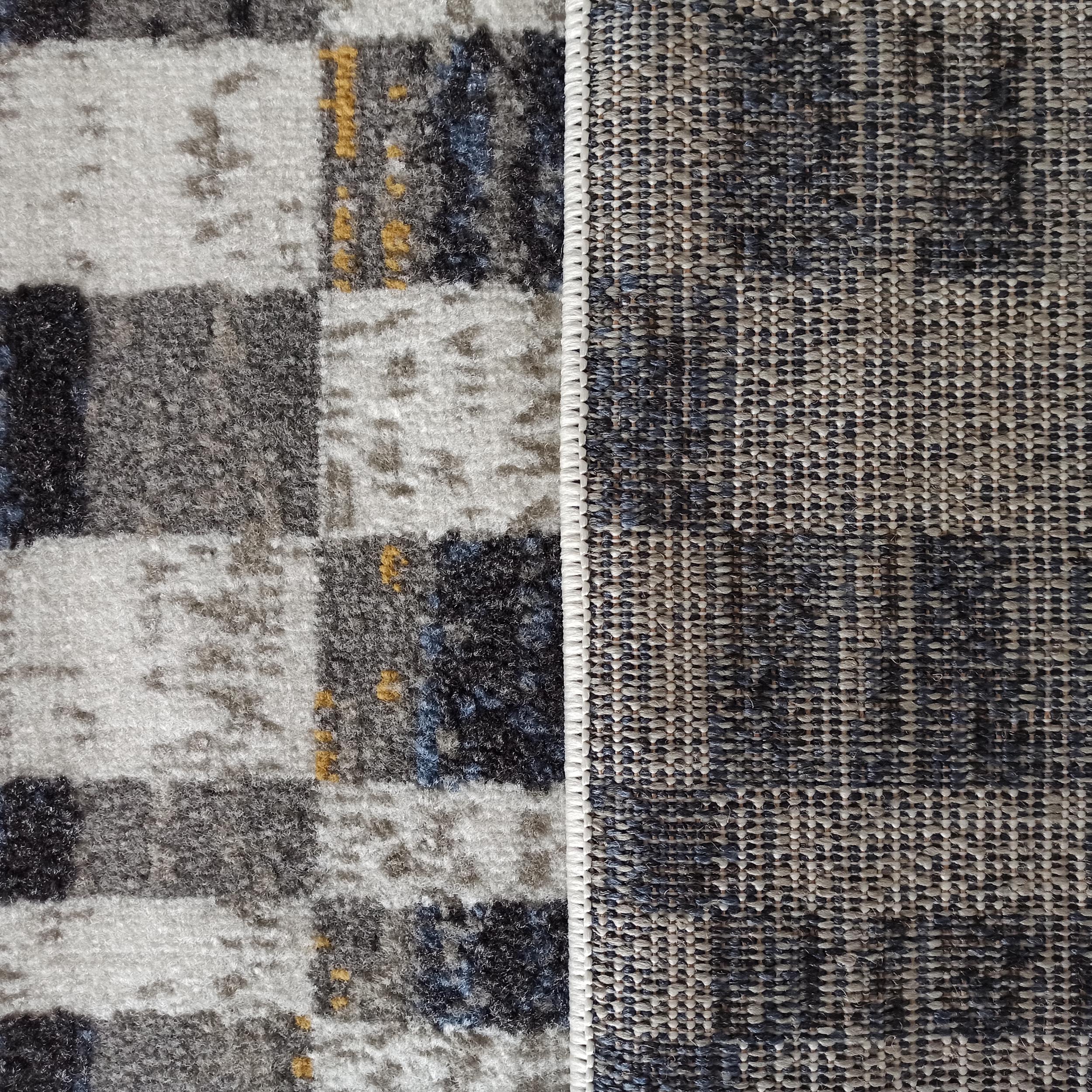 Tapis présentant une surface douce et mouchetée de gris, blanc, bleu et ocre, et son revers tissé à mailles serrées