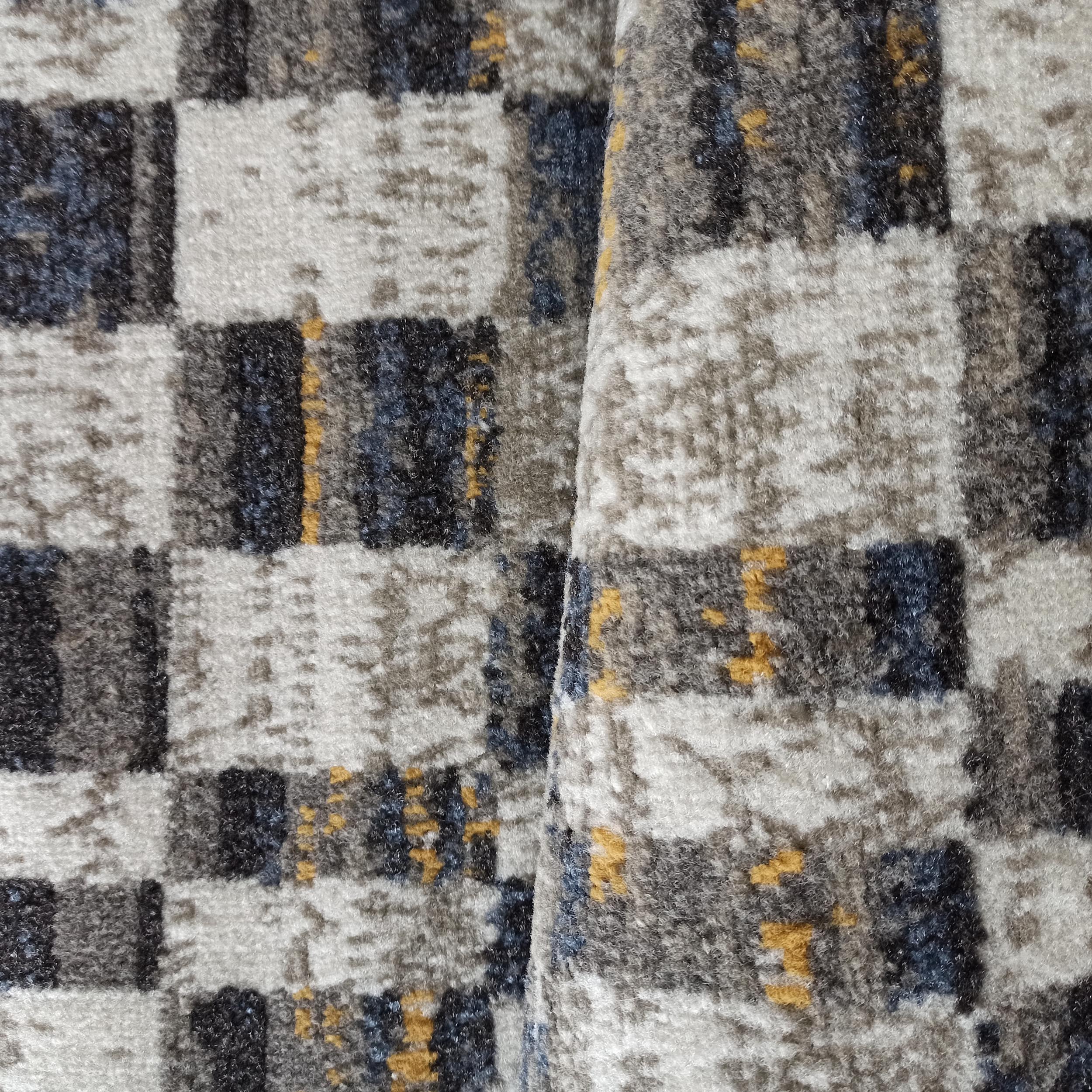 Tapis à texture douce et dense, avec un motif abstrait de carreaux mêlant des nuances de gris, noir, bleu et jaune
