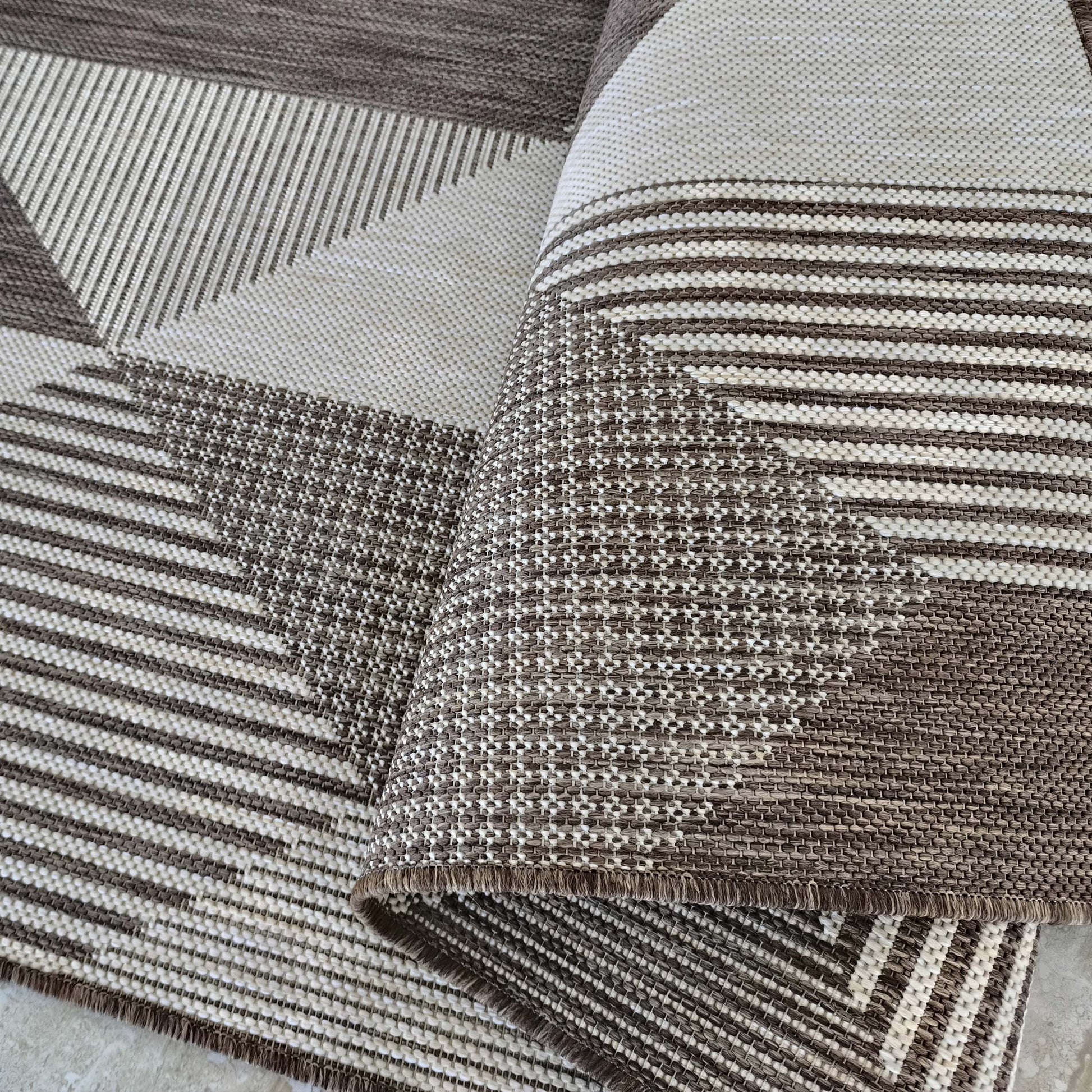 Tapis tissé à motifs géométriques de rayures et de triangles en brun et beige, avec différentes textures, une partie est enroulée