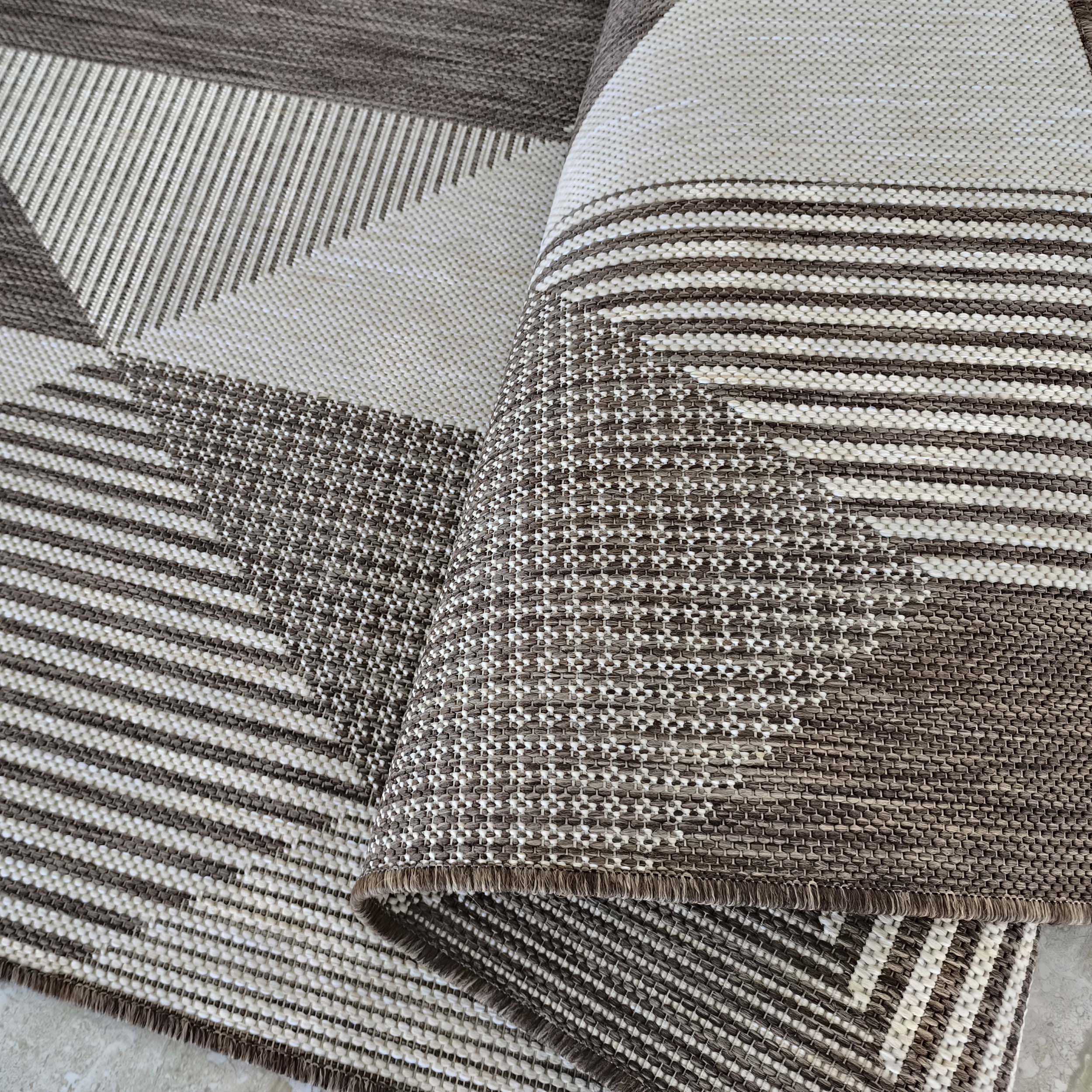Tapis tissé à motifs géométriques de rayures et de triangles en brun et beige, avec différentes textures, une partie est enroulée
