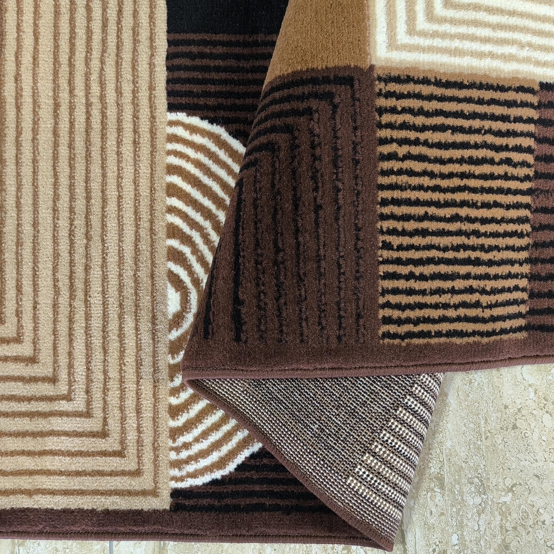 Tapis texturé aux motifs géométriques divers marron, beige, noir et crème, une partie est pliée montrant son envers