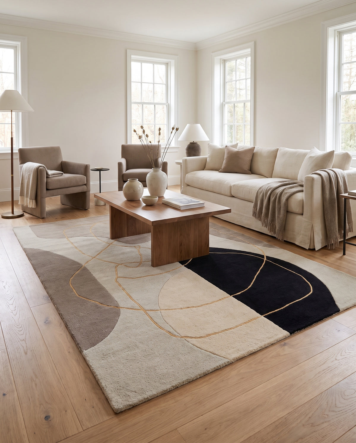 Au sol, un tapis en laine sculptée aux formes abstraites beige, taupe et noir, avec des lignes dorées en relief