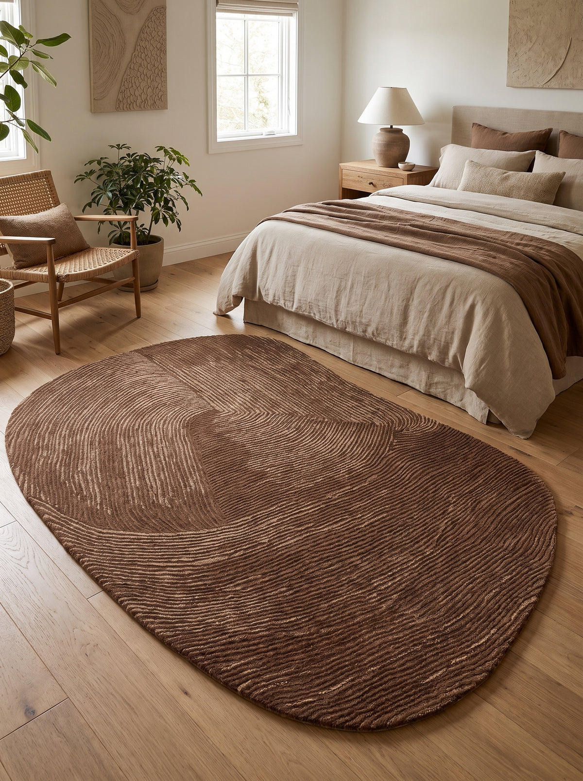 Les ondes texturées du tapis ovale organique en laine et coton, brun chocolat et beige, sont posées dans une chambre claire