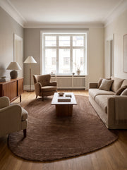 Des lignes sinueuses brun chocolat et beige marquent ce tapis ovale organique en laine et coton posé dans un salon clair