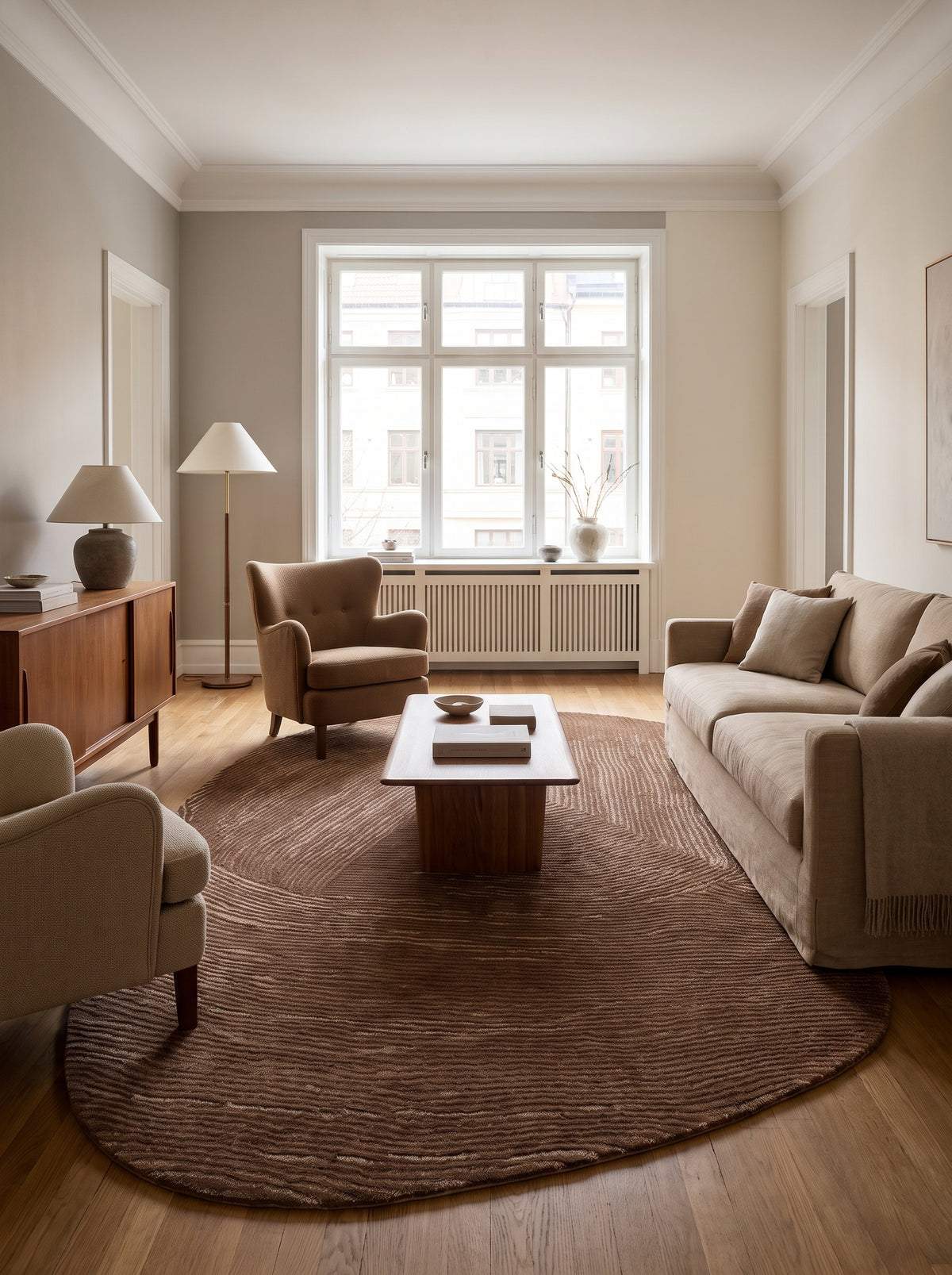 Des lignes sinueuses brun chocolat et beige marquent ce tapis ovale organique en laine et coton posé dans un salon clair