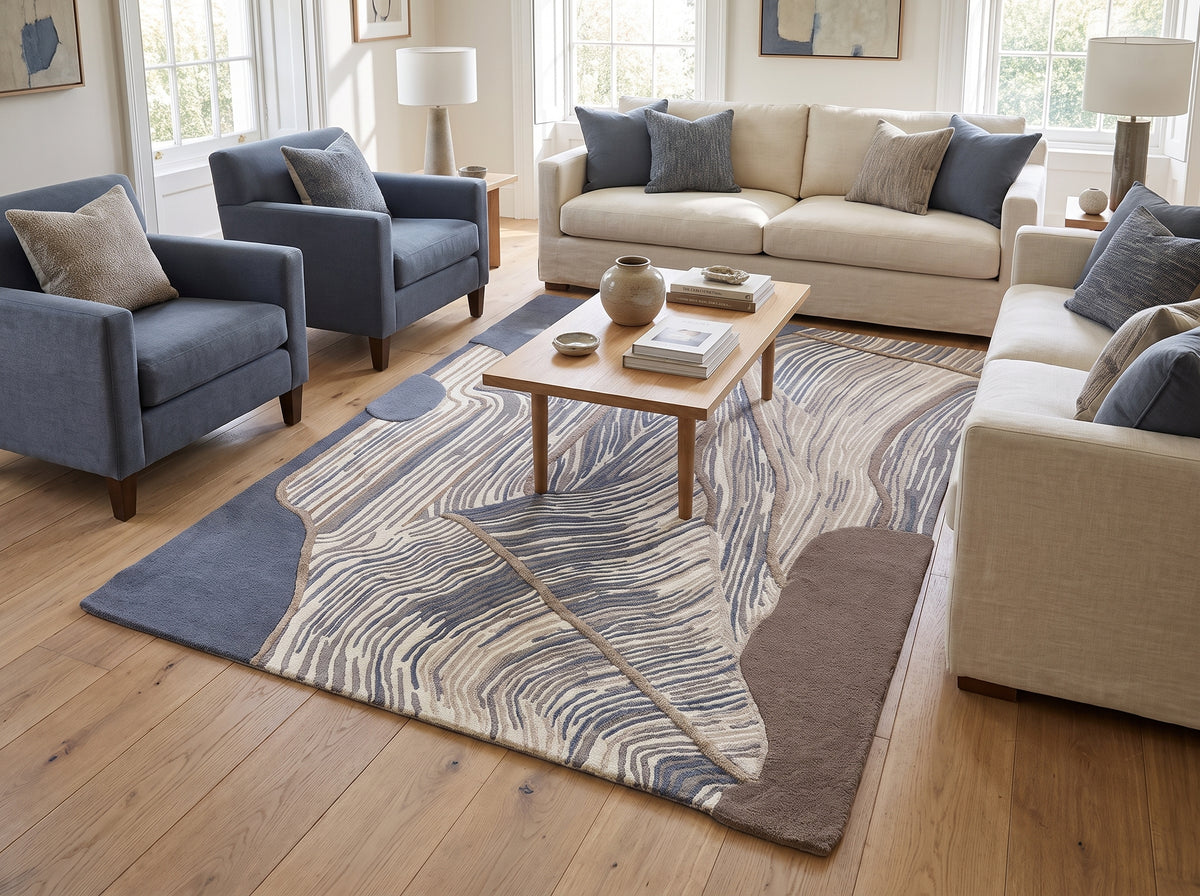 Ce tapis en laine et viscose fait main combine motifs abstraits en relief et aplats bleu acier, crème et brun dans un salon