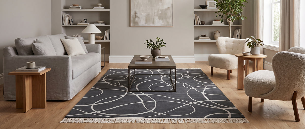 Gris anthracite en laine et viscose, ce tapis aux courbes argentées sculptées et franges est posé dans un salon