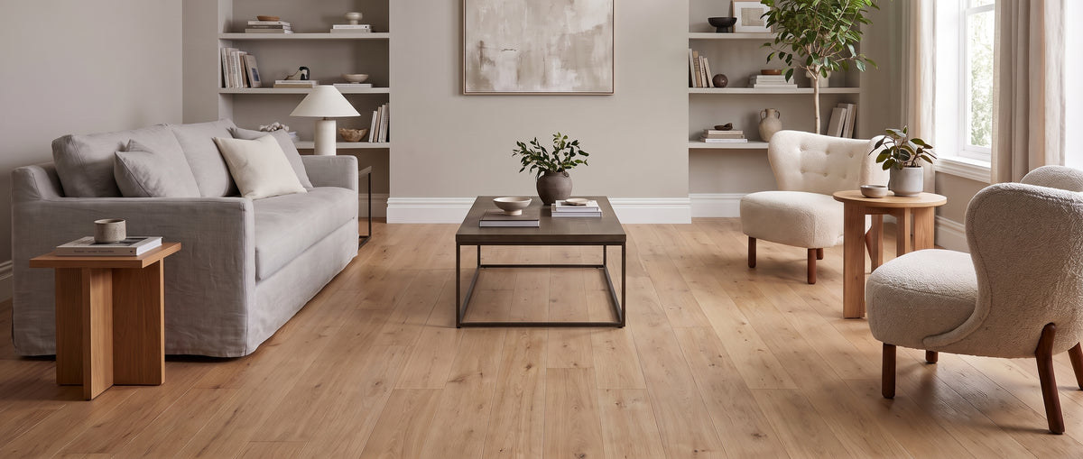 Pièce à vivre lumineuse, sol en parquet clair sans tapis, avec un canapé gris, des fauteuils écrus et des étagères