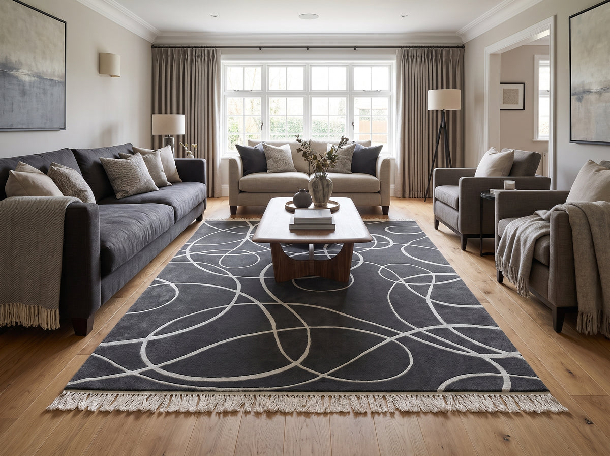 Gris anthracite et argenté, ce tapis en laine et viscose tufté main aux courbes sculptées et franges claires habille un salon