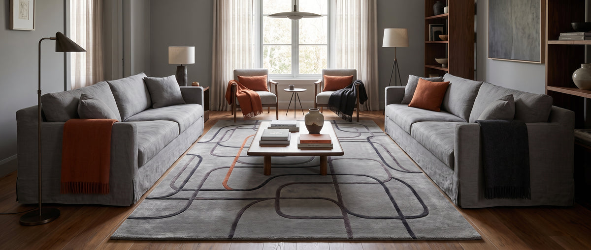Tufté main, ce tapis laine et viscose gris révèle des pistes arrondies anthracite et cuivre en relief dans un salon