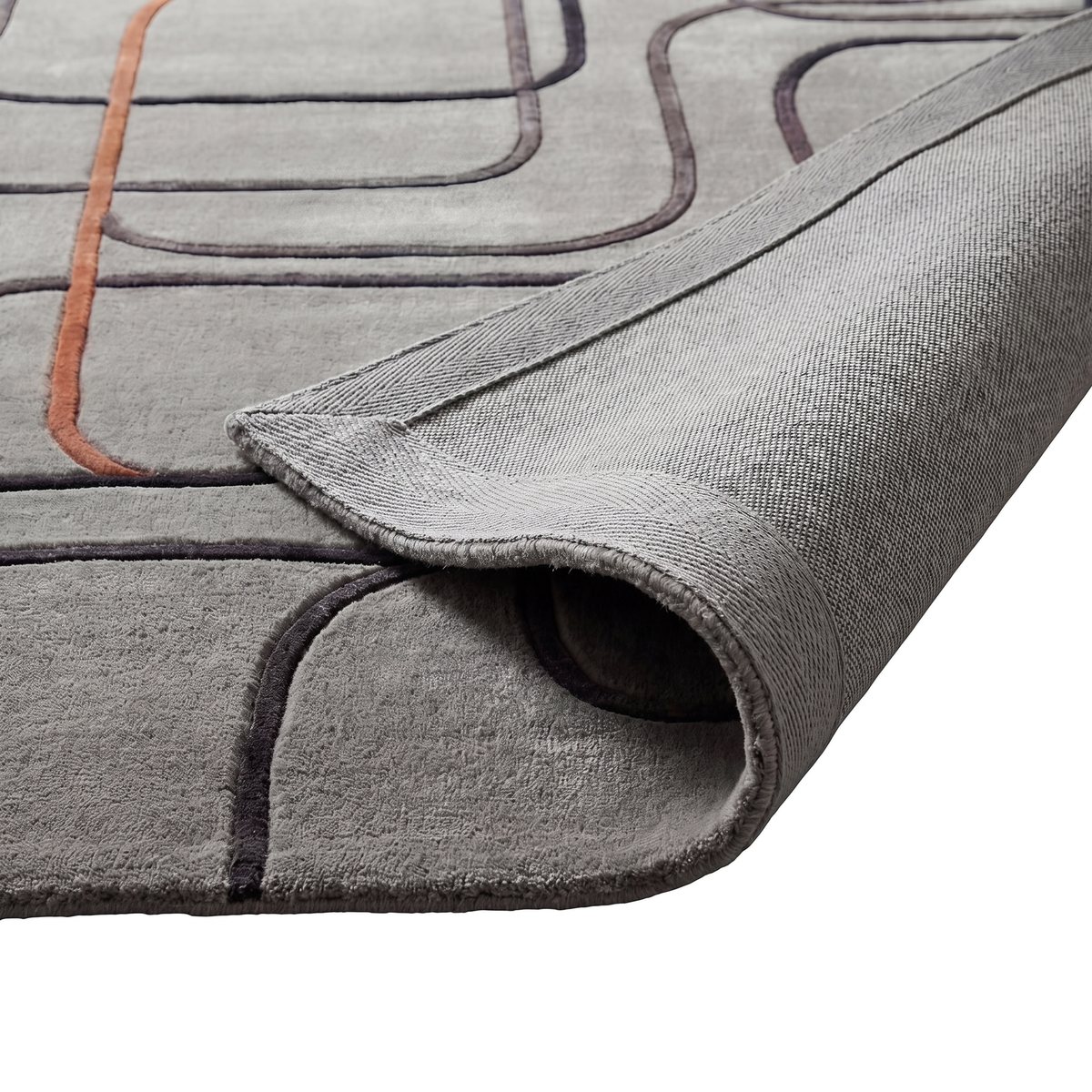La texture du velours coupé, les motifs anthracite et cuivre en relief, et l'envers tissé du tapis laine et viscose