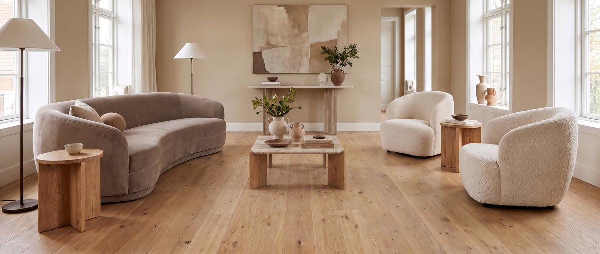 Un canapé courbé et des fauteuils bouclés meublent ce salon aux tons clairs, présenté sans tapis sur son parquet nu