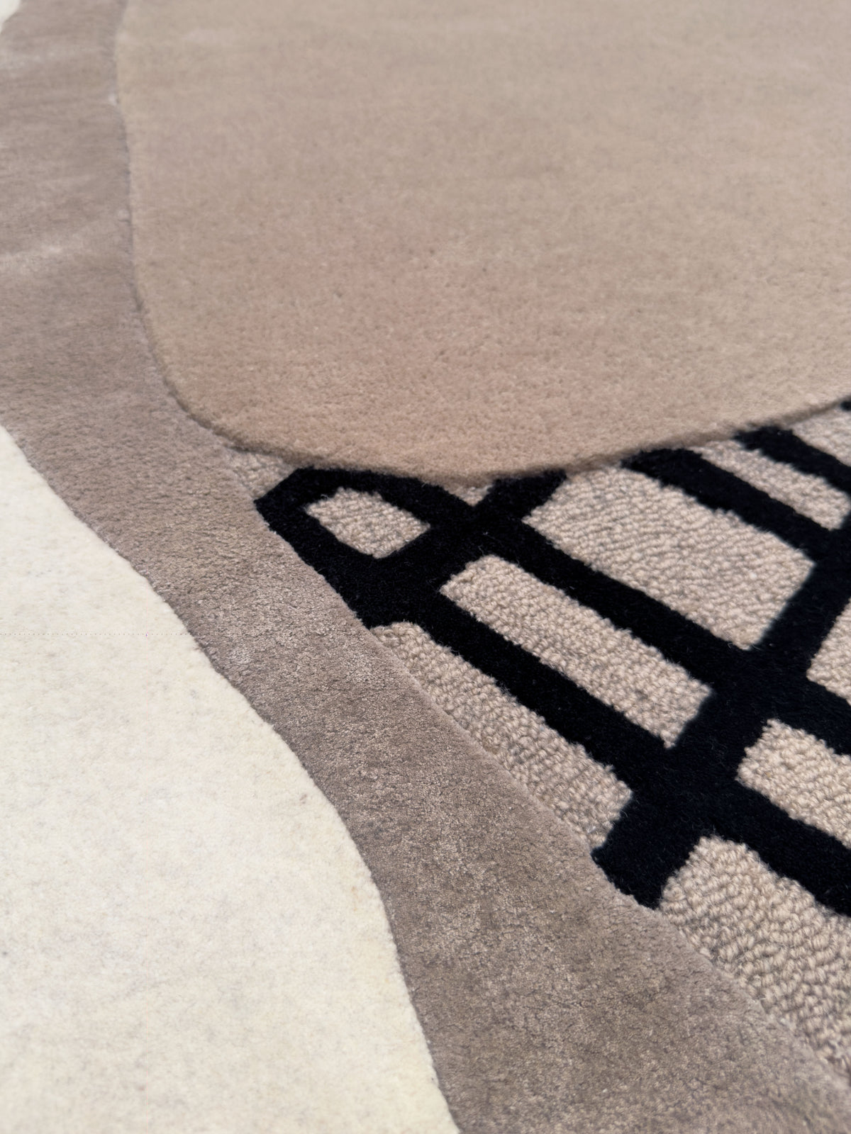 La texture d'un tapis fait main en laine et viscose, avec ses bouclettes noires et son velours rasé gris et taupe
