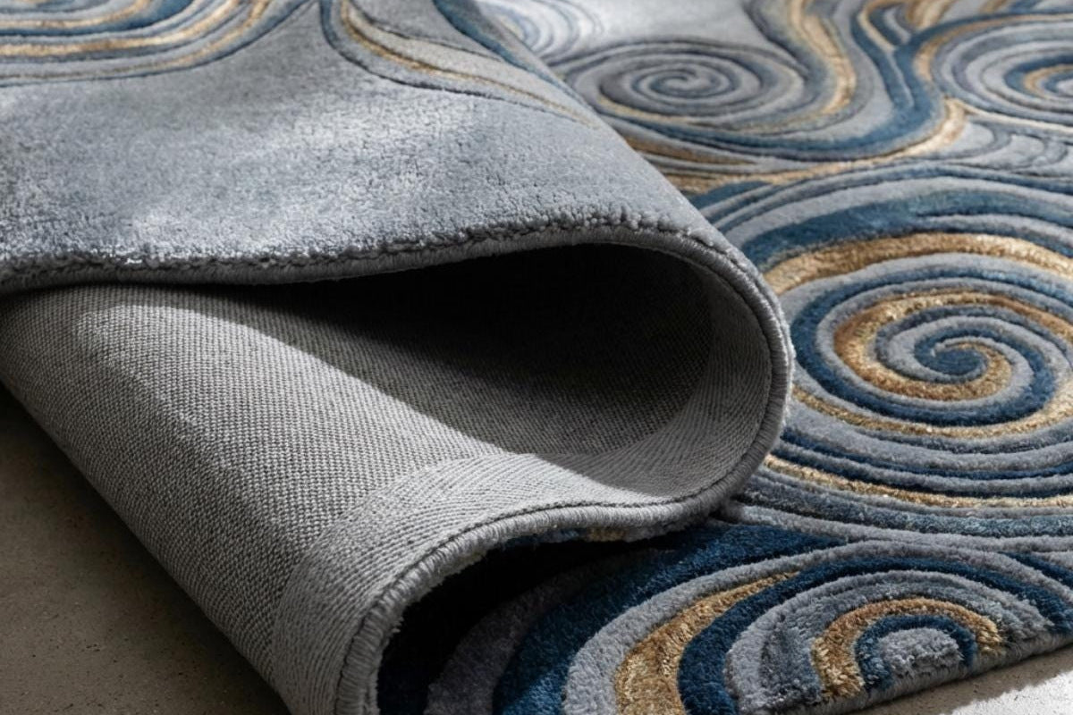 Pli d'un tapis en laine et viscose aux spirales bleu nuit et or en relief, avec son envers gris tissé visible