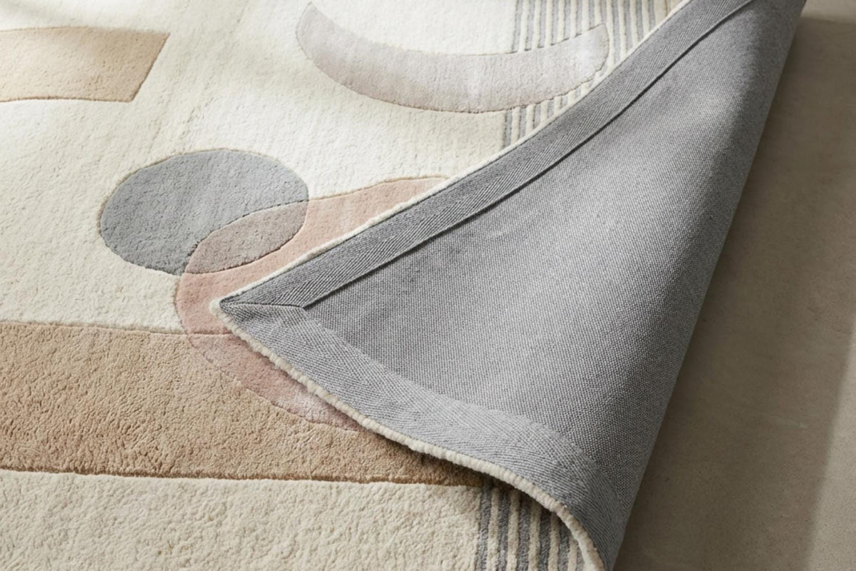 Coin relevé d'un tapis en laine et viscose ivoire à formes gris bleu et rose poudré, dévoilant son envers gris