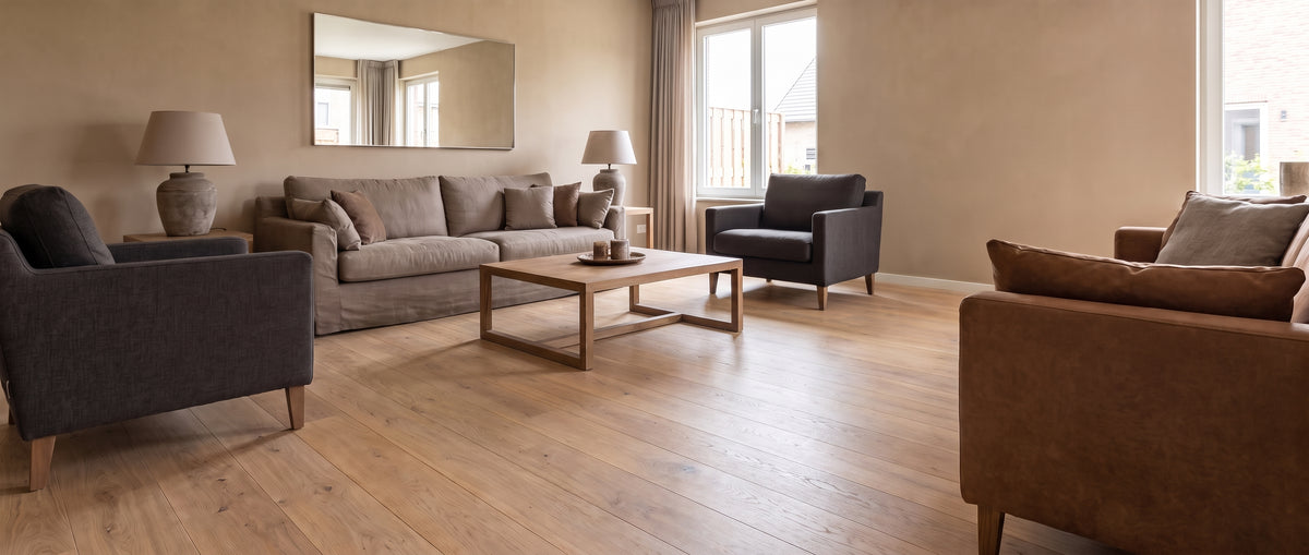 Le parquet clair et nu d'un salon lumineux est montré sans tapis, agrémenté de canapés, fauteuils et table basse