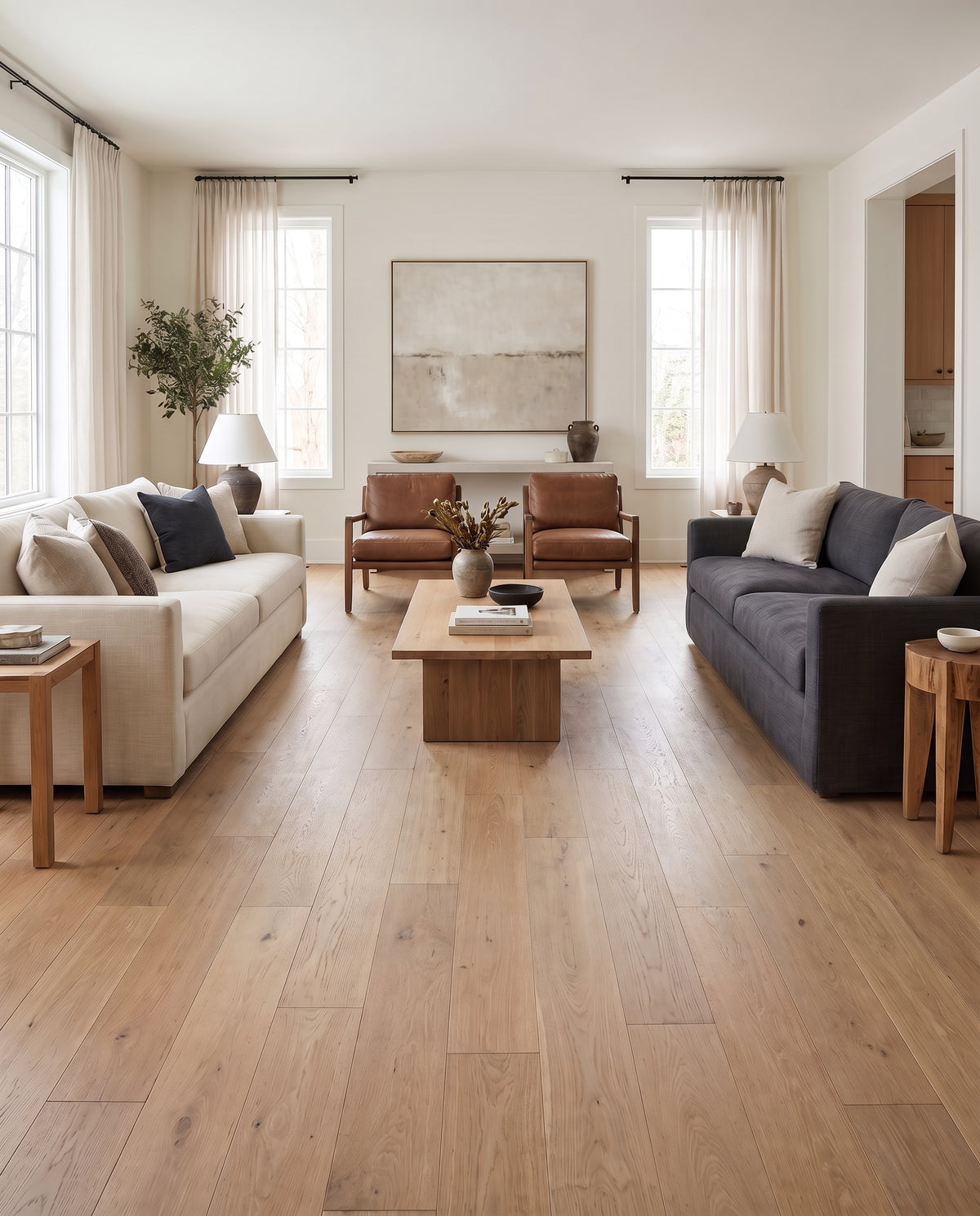 Pièce de vie lumineuse au sol nu, sans tapis, présentant deux canapés, fauteuils en cuir et table basse en bois massif