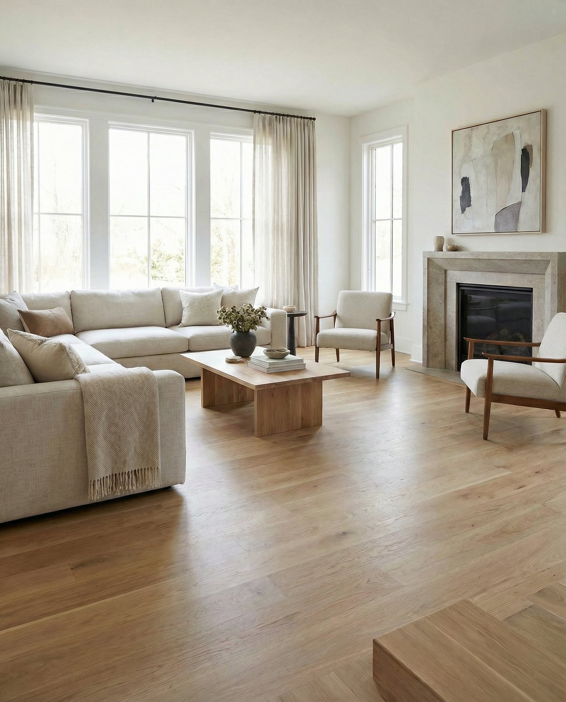 Pièce lumineuse avec plancher en bois clair, canapé beige, fauteuils et cheminée. Ambiance neutre et relaxante. Espace à