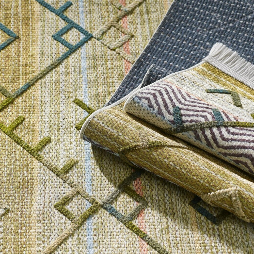 Tapis superposés aux textures et motifs variés. Un tapis vert et beige à motifs géométriques, un tapis roulé à rayures et franges, et un tapis bleu à pois