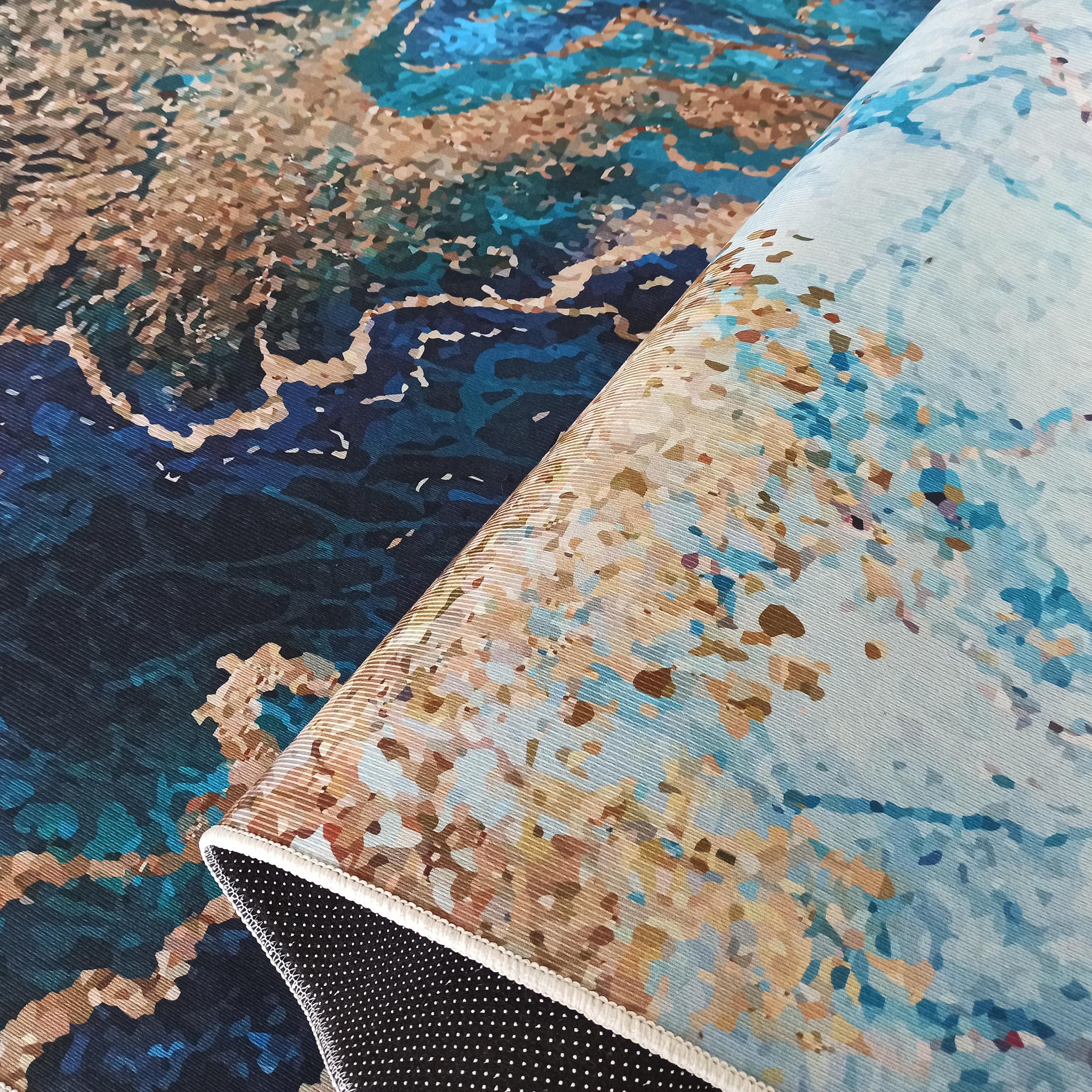 Tapis aux motifs abstraits onduleux bleus, turquoises et dorés. Une partie est roulée, montrant son envers noir à pois blancs