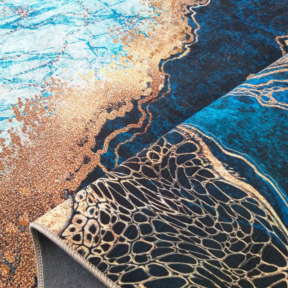 Tapis abstrait aux motifs onduleux marins et minéraux, mêlant bleus clairs et foncés, doré et cuivré, avec une partie roulée