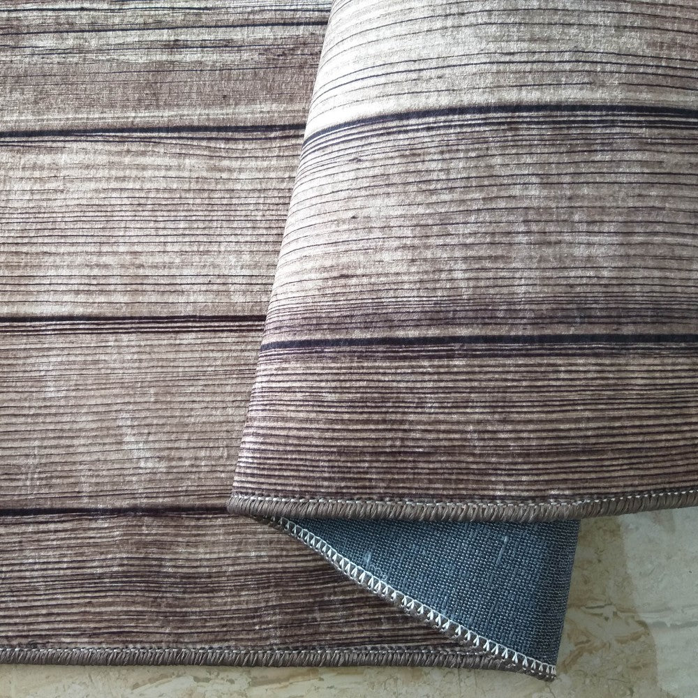 Tapis marron clair avec des motifs de veinures de bois sombres Il est partiellement roulé, révélant son envers bleu-gris et une bordure cousue
