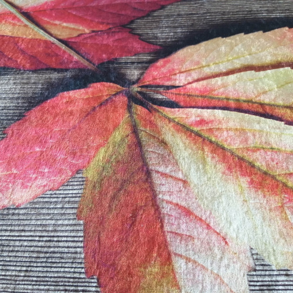 Tapis doux à motifs de feuilles d'automne rouges, orangées et jaunes, posées sur un fond sombre évoquant du bois