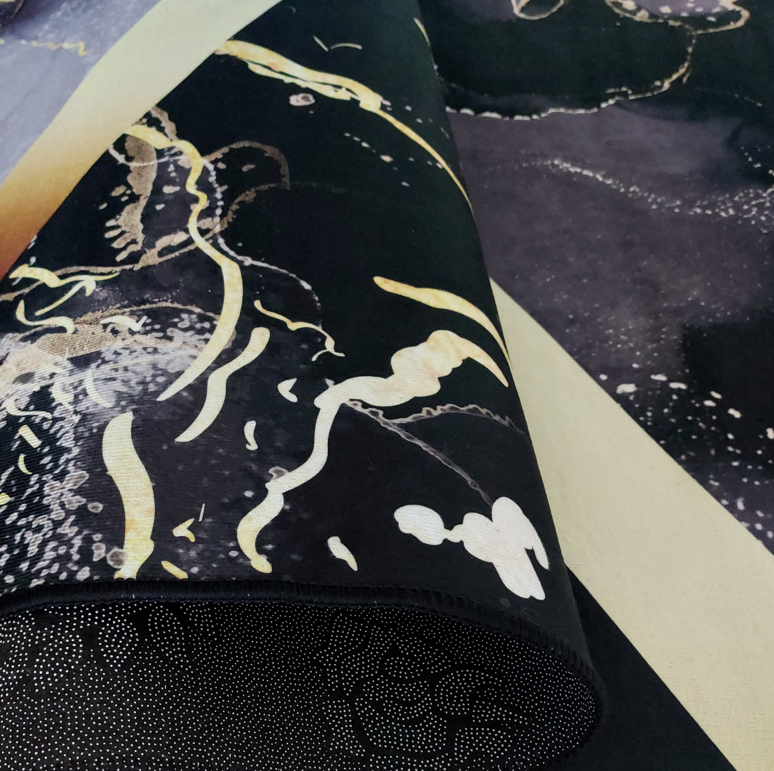 Tapis partiellement roulé montrant des motifs abstraits noirs, dorés et blancs, une zone beige et le dessous antidérapant