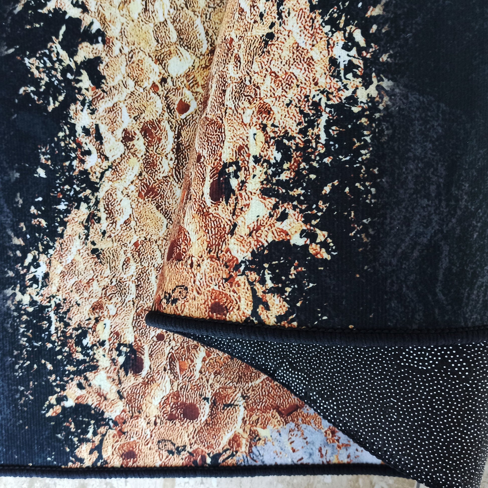 Tapis aux motifs abstraits et texturés noir, orange rouille et crème, dont l'envers antidérapant noir à points blancs est exposé