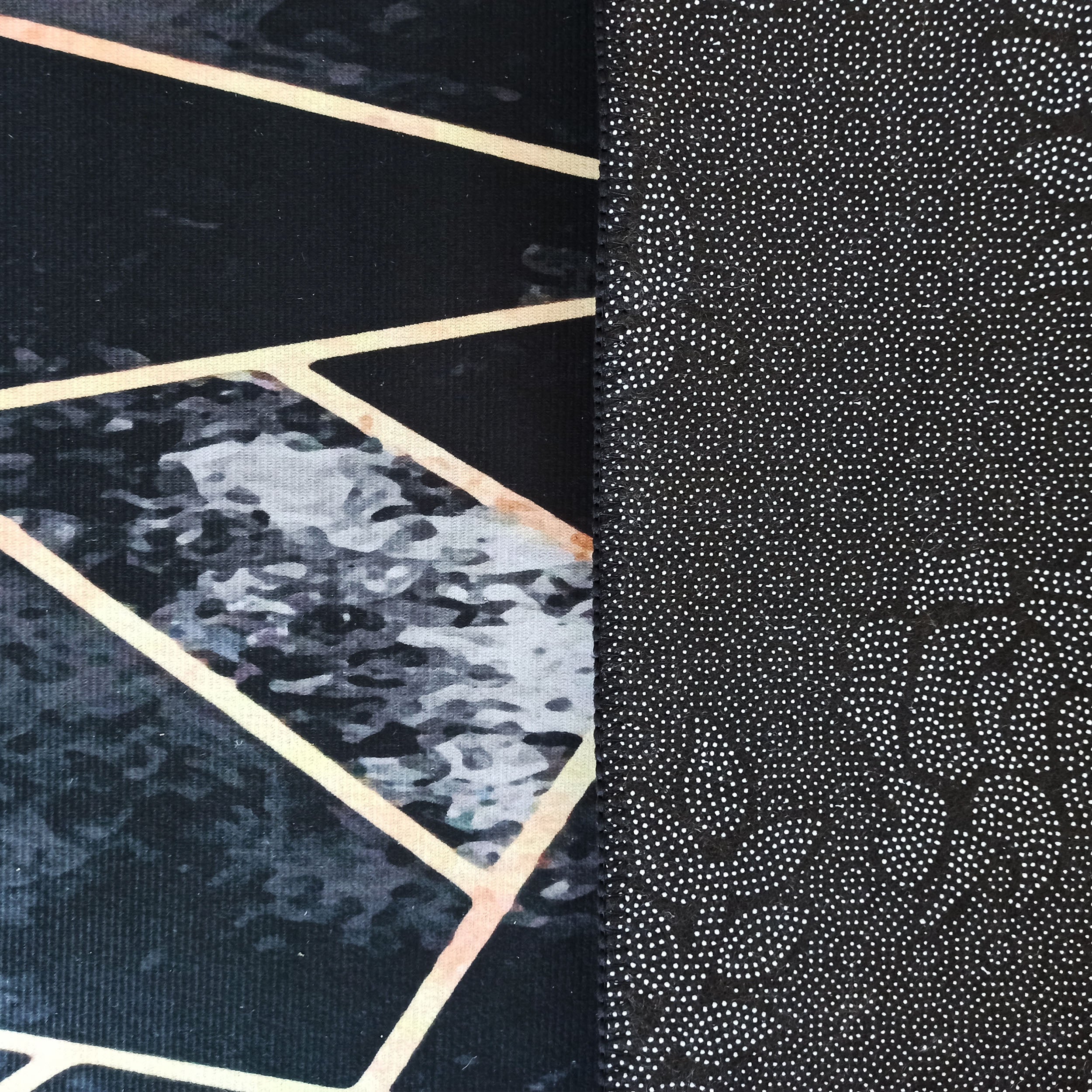 Tapis montrant un côté face noir à motifs géométriques dorés et marbrés gris, et un côté verso noir à picots blancs