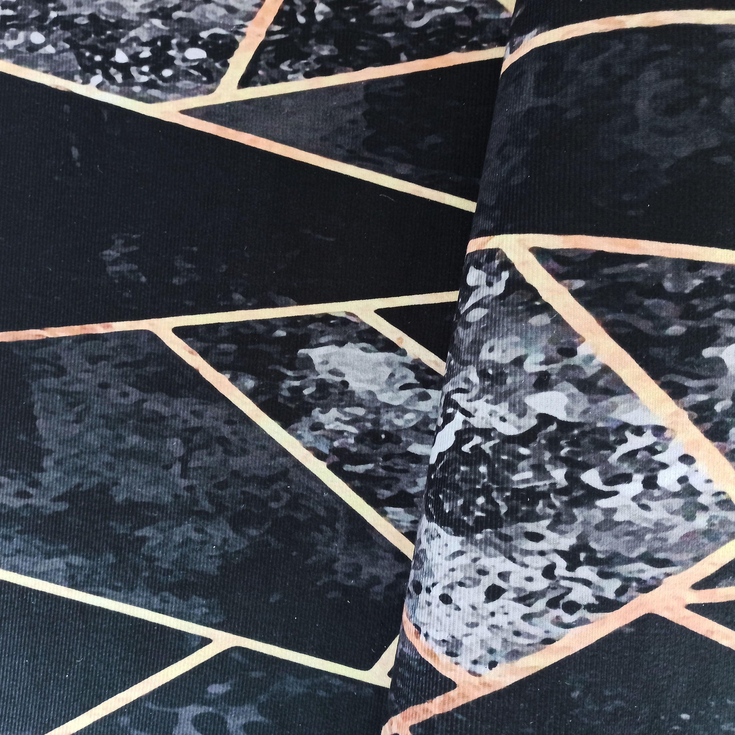 Tapis avec motif géométrique de lignes dorées et texture marbrée grise sur fond noir, partiellement plié