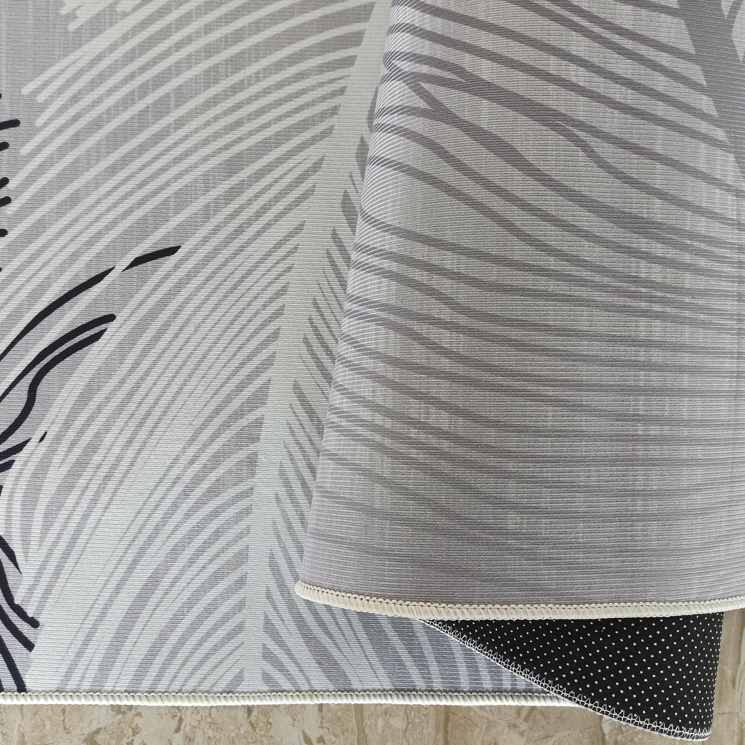 Tapis gris aux motifs abstraits blancs et noirs, surface côtelée visible, bordure tressée et envers noir à pois blancs