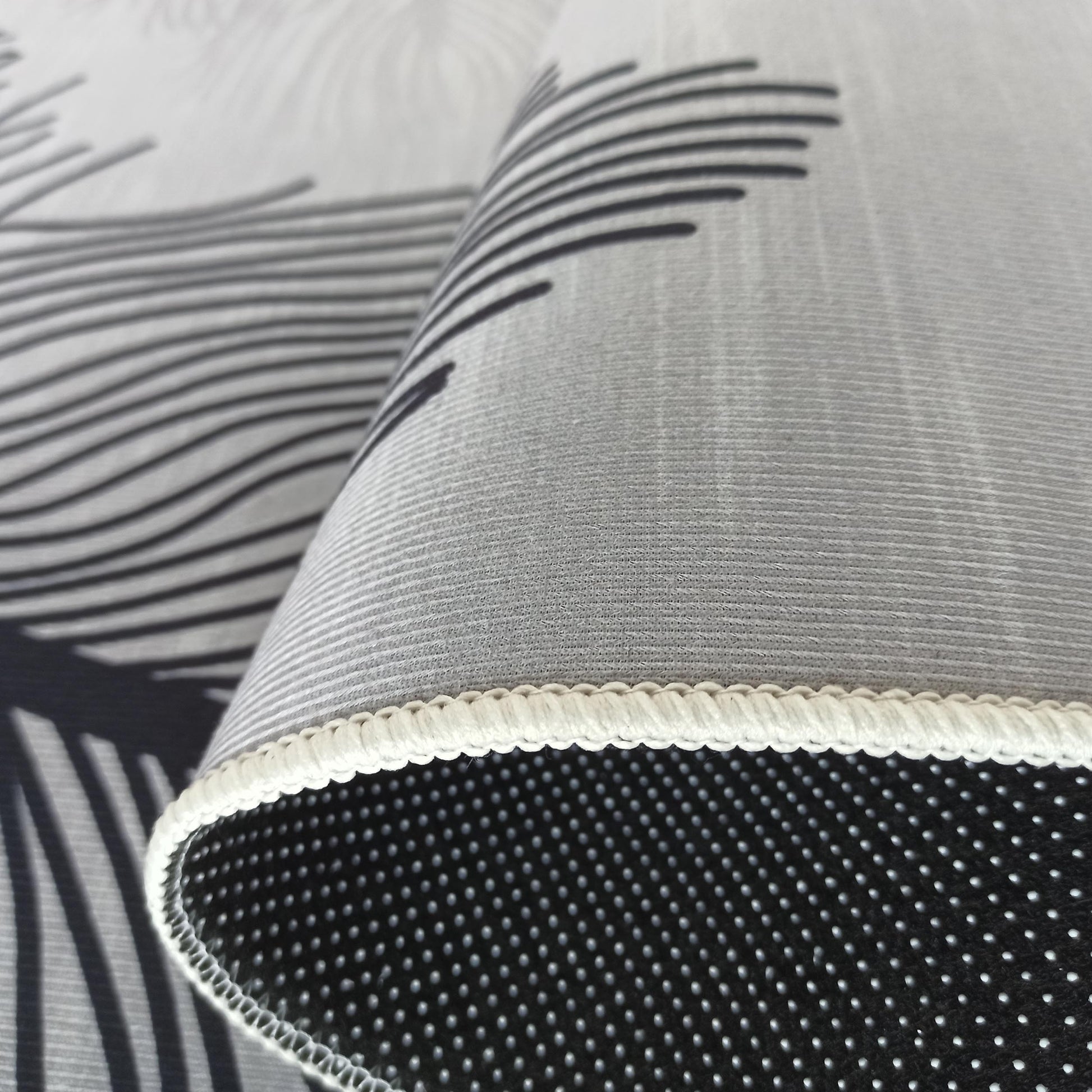 Tapis roulé blanc et gris avec des motifs de lignes noires, son dessous noir antidérapant et son bord surpiqué