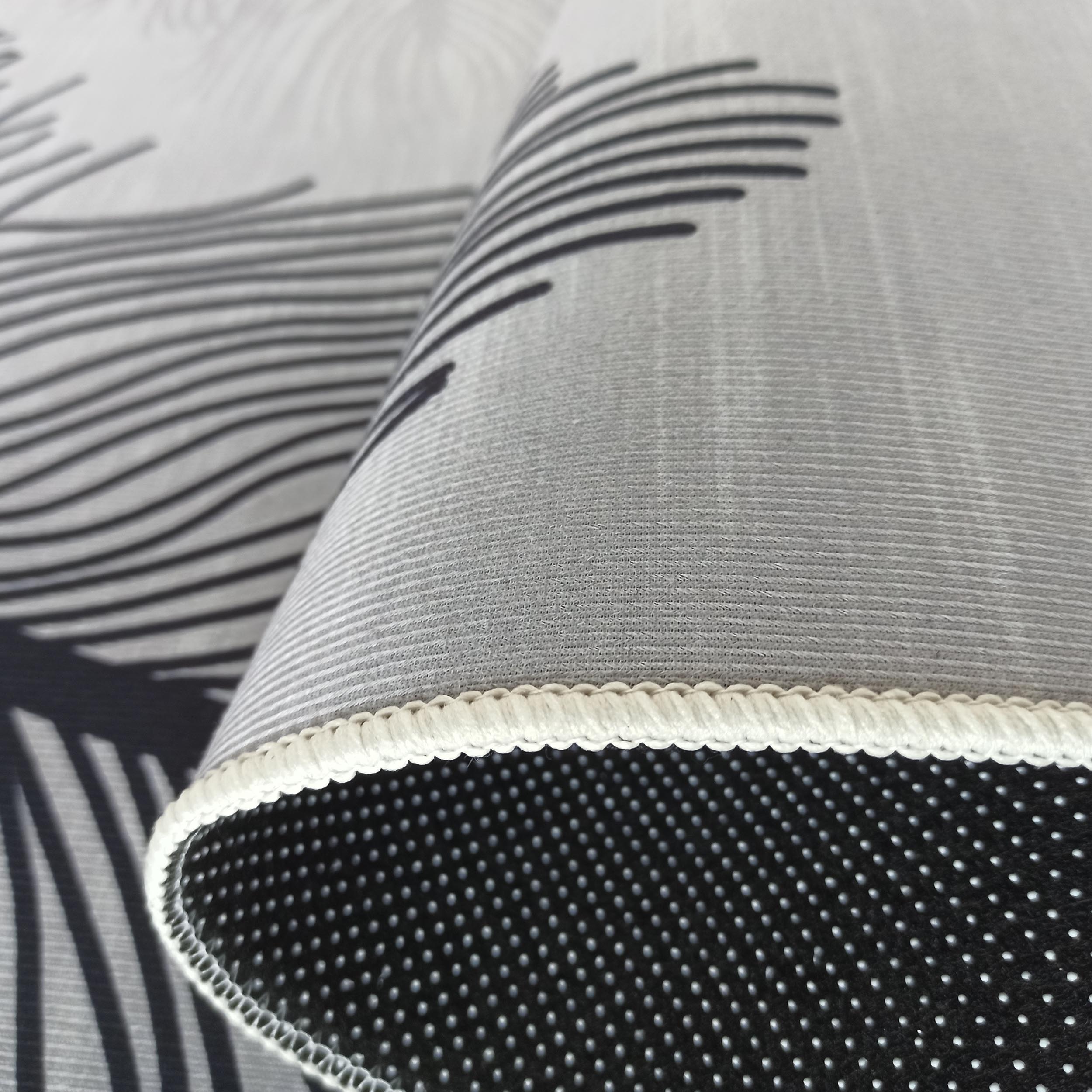 Tapis roulé blanc et gris avec des motifs de lignes noires, son dessous noir antidérapant et son bord surpiqué