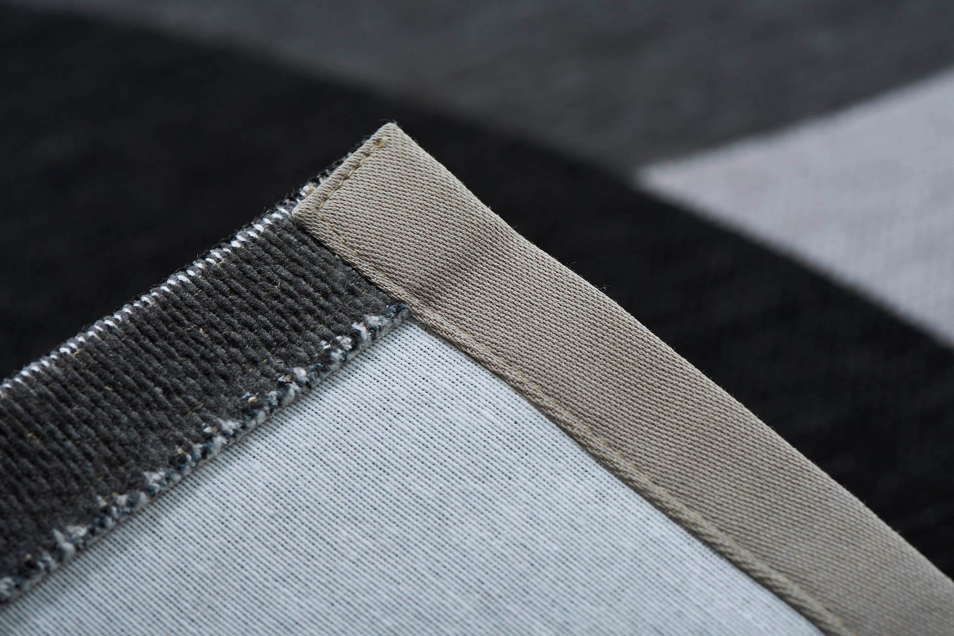 Gros plan sur un tapis lavable géométrique gris, montrant les fibres et la couture de finition, parfait pour décorer votre intérieur.
