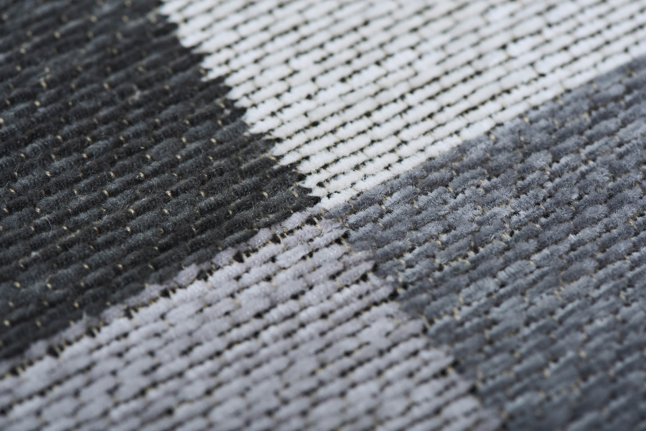 Gros plan d'un tapis rectangulaire. Tissage en relief, aspect tactile. Bordure beige. Couleurs grises