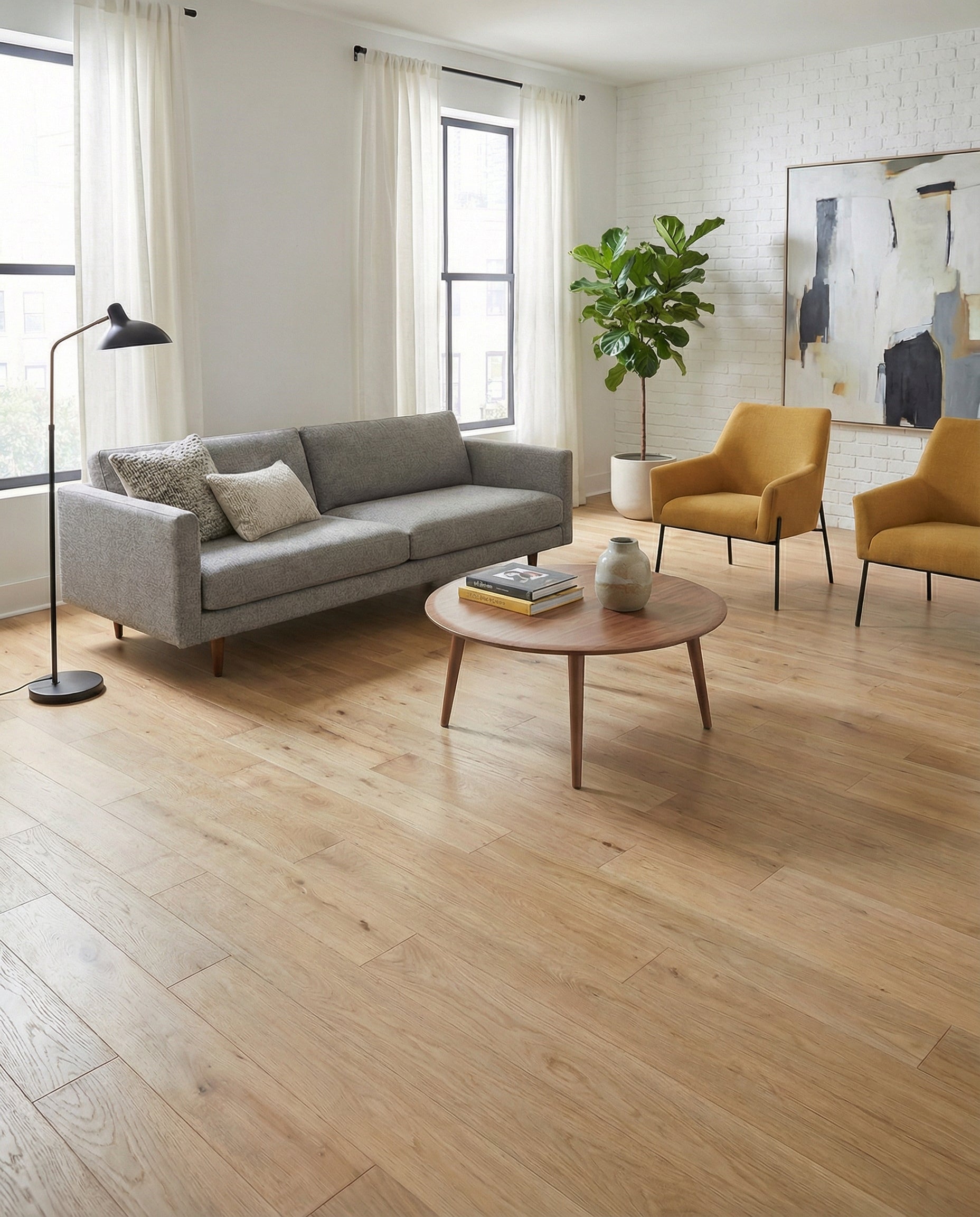 Pièce lumineuse avec parquet clair, canapé gris, fauteuils jaunes, table ronde. Ambiance chaleureuse et moderne. Espace à