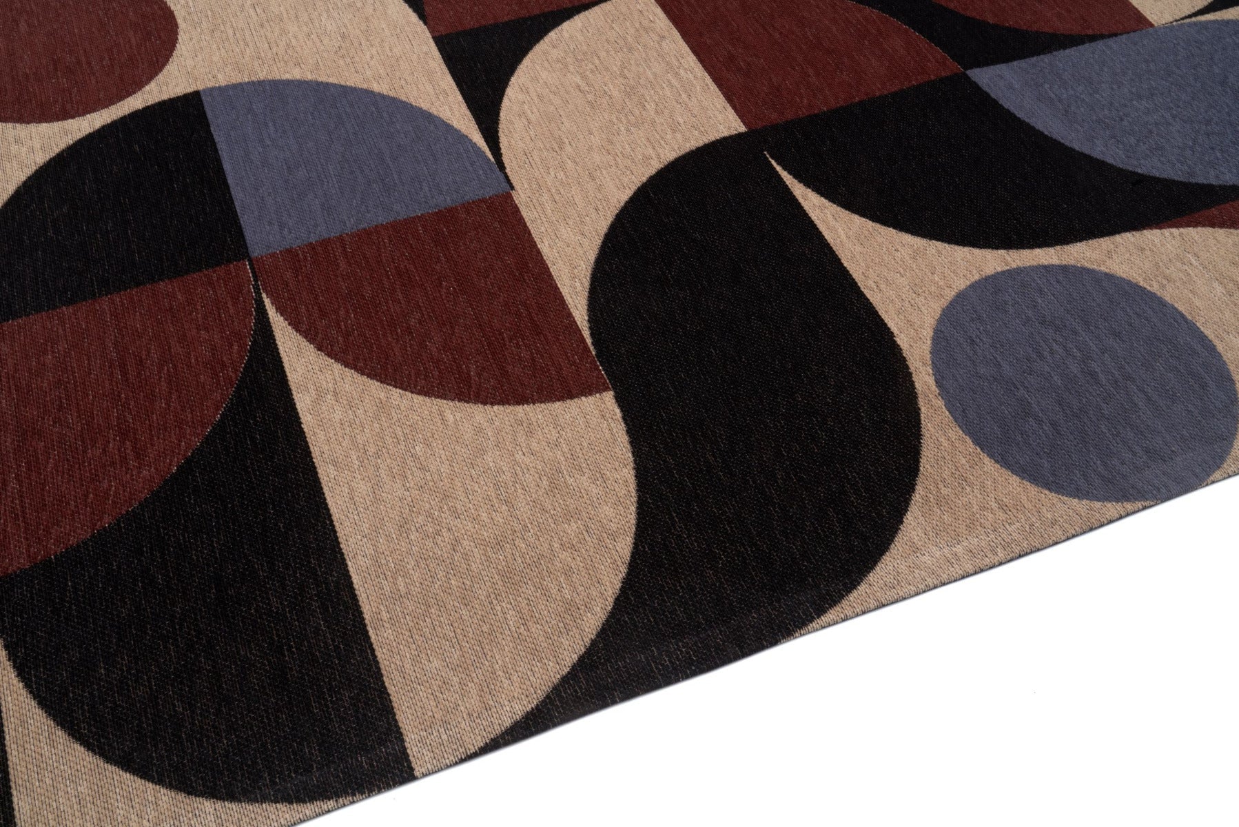 Gros plan sur un tapis géométrique multicolore, avec des formes sombres, des cercles bleus et des touches de beige et marron.