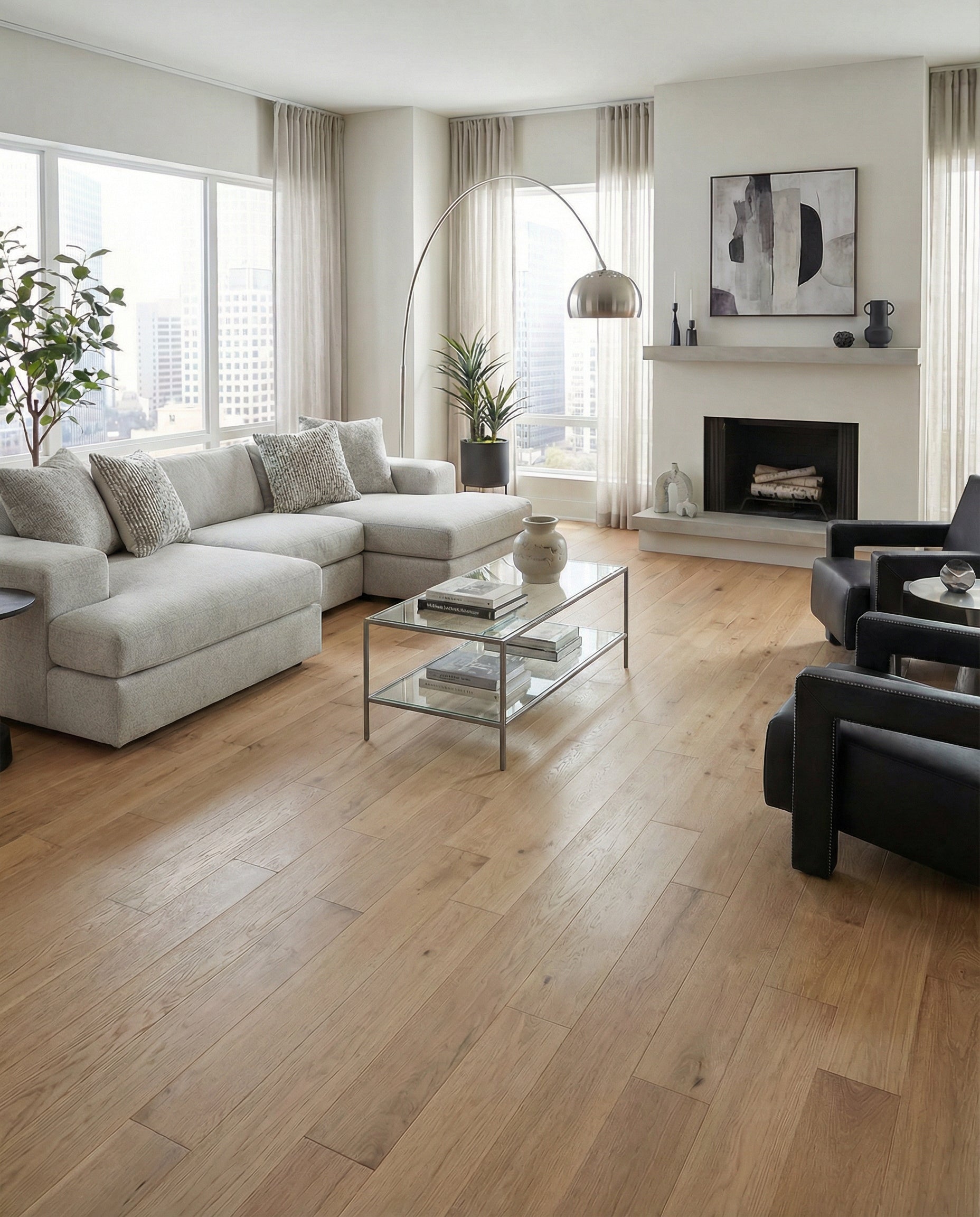 Pièce lumineuse avec plancher en bois clair, canapé gris, fauteuils noirs, cheminée. Espace à transformer