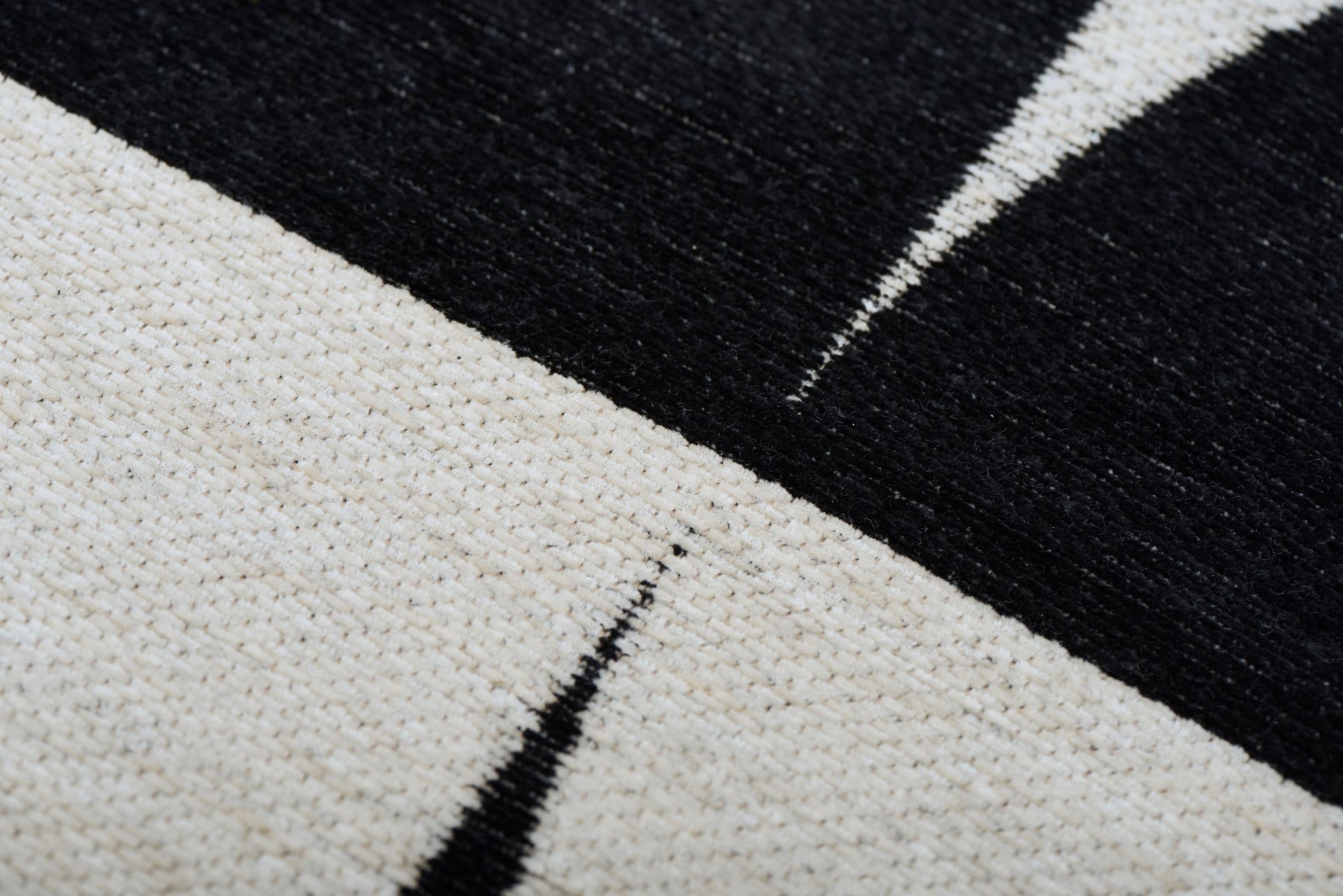 Gros plan sur un tapis rectangulaire. Tissage en relief, aspect tactile et doux. Alternance de bandes beige et noires