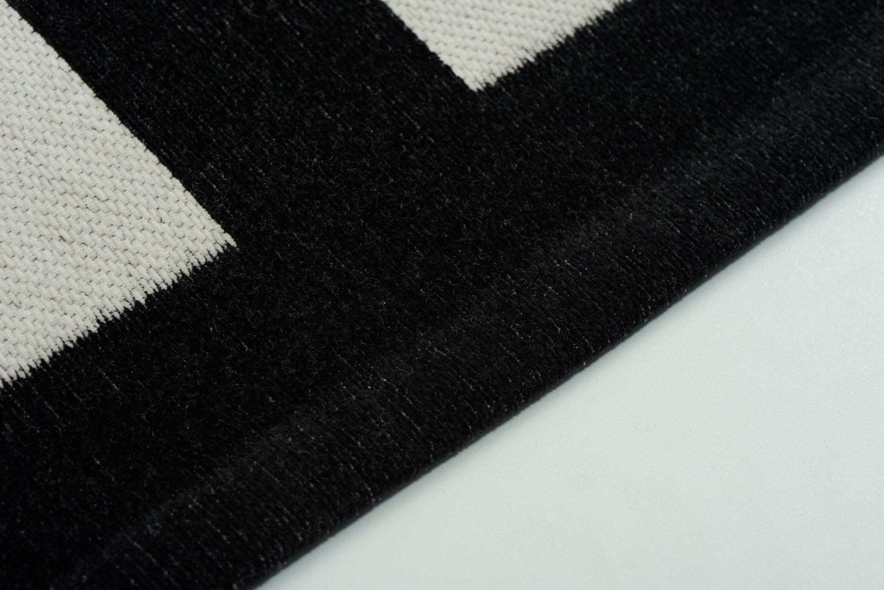 Tapis noir et blanc, tissage plat. Surface texturée, aspect tactile. Forme rectangulaire. Ambiance sobre