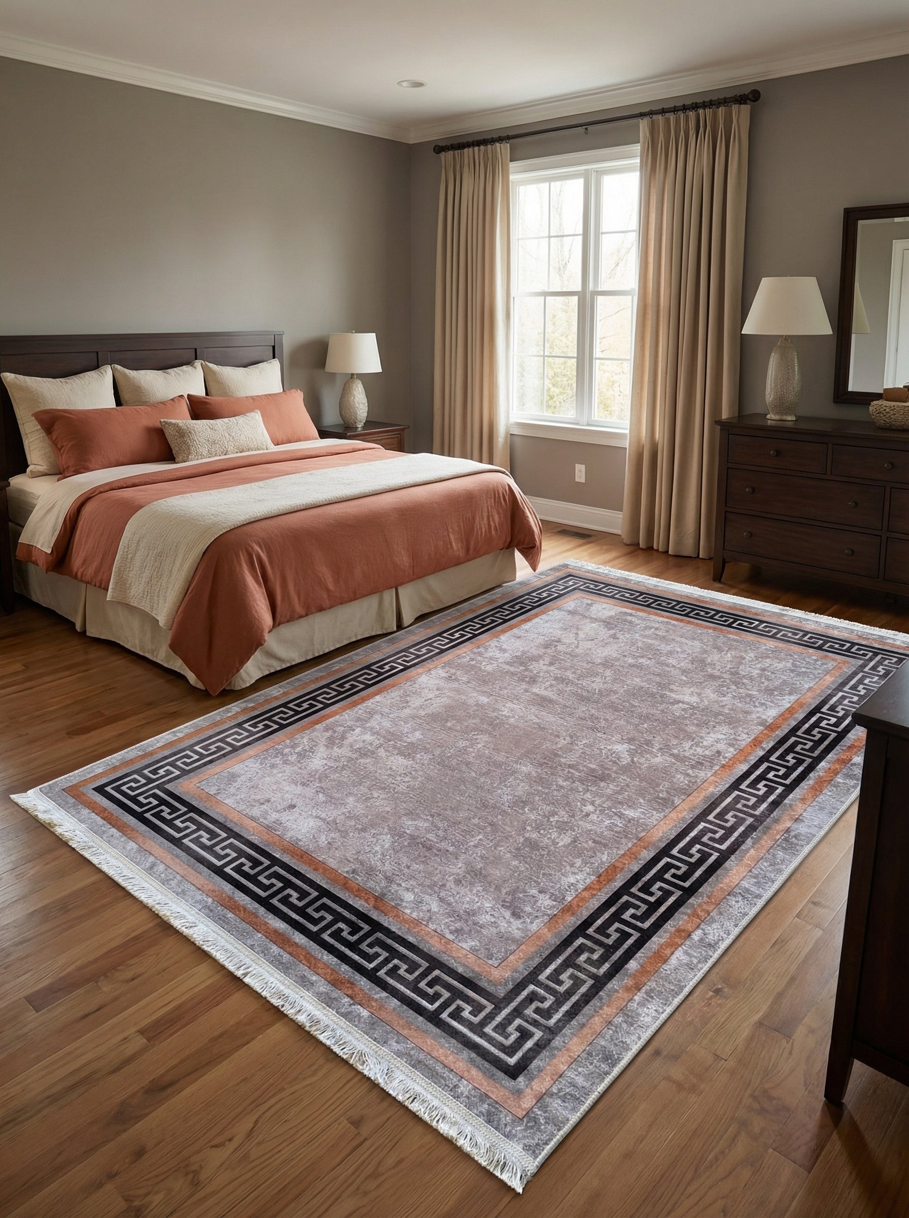 Tapis rectangulaire gris-beige texturé avec une bordure méandre noire et cuivre, posé sur un parquet dans une chambre à coucher